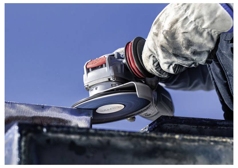 Eine Person mit Handschuhen verwendet einen Winkelschleifer, um eine Metalloberfläche vor einem klaren blauen Himmelshintergrund zu schneiden oder zu glätten.