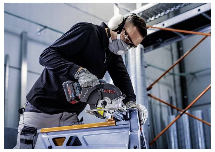 Ein Arbeiter, der eine Kreissäge zum Schneiden von Metall verwendet, trägt Sicherheitsausrüstung wie Schutzbrille, Gehörschutz und Maske in einer industriellen Umgebung.