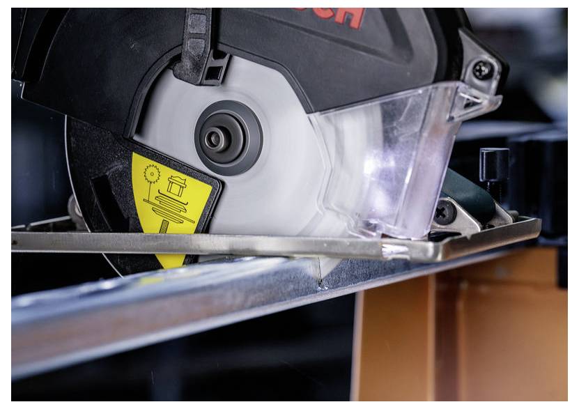 Eine Kreissäge, die durch einen Metallstab schneidet, mit sichtbarem Sicherheitswarnschild an der Schutzvorrichtung.