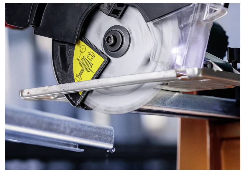 Eine Kreissäge, die aktiv einen Metallträger durchschneidet, wobei Funken und Bewegung sichtbar sind, mit Sicherheitshinweisen, die an der Säge angebracht sind.