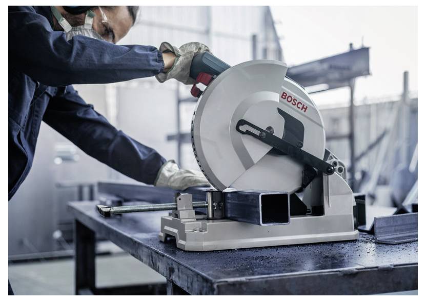 Eine Person in Schutzausrüstung bedient eine Bosch-Metalltrennkreissäge auf einem rechteckigen Stahlträger in einer Industriewerkstatt.
