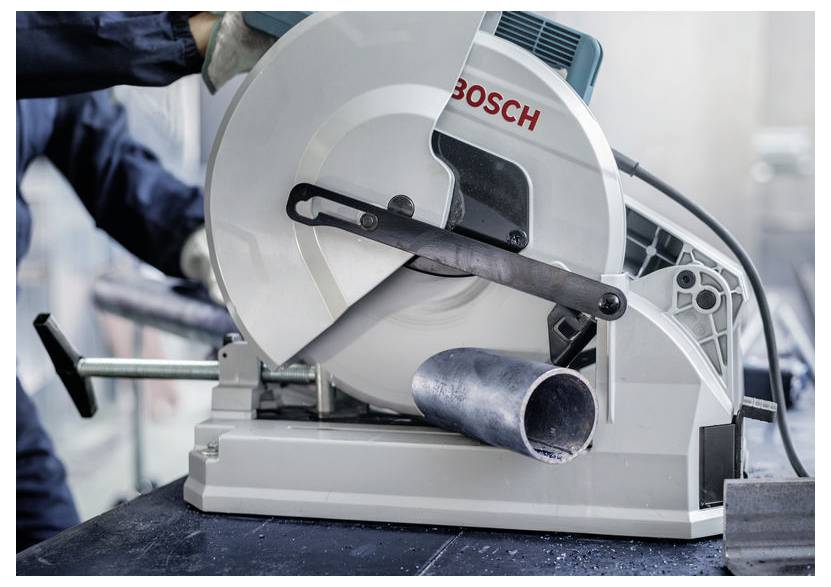 Eine Person bedient eine Bosch-Metalltrennkreissäge und schneidet dabei ein Metallrohr. Die Umgebung wirkt industriell und deutet auf Reparatur- oder Bauarbeiten hin.