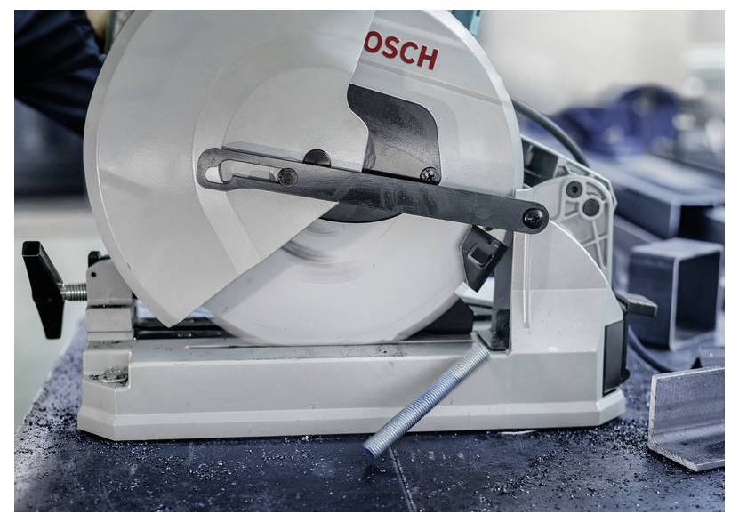 Eine Kreissäge in Betrieb, die durch einen Metallstab schneidet. Die Säge ist eine Bosch-Marke und wird in einer industriellen Umgebung mit Metallspänen in der Nähe gezeigt.