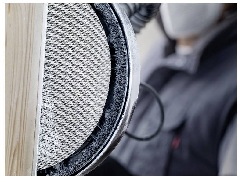 Eine Person in Schutzausrüstung benutzt einen elektrischen Schleifer auf einer Holzoberfläche und unterstreicht damit Holzarbeiten oder Zimmermannsarbeiten in Gange.