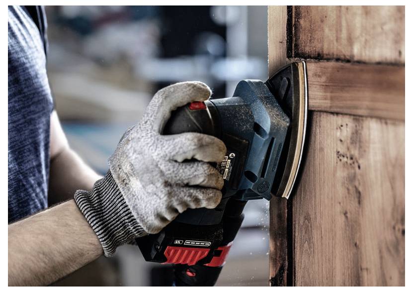 Eine Person mit Handschuhen benutzt einen elektrischen Schleifer an einer Holztür und glättet deren Oberfläche.