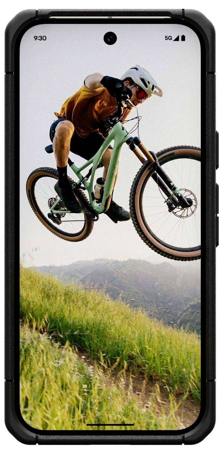 Eine Person mit Helm führt auf einem Mountainbike einen Sprung vor einer Kulisse von Hügeln und klarem Himmel aus und demonstriert dynamische Action und Sport.