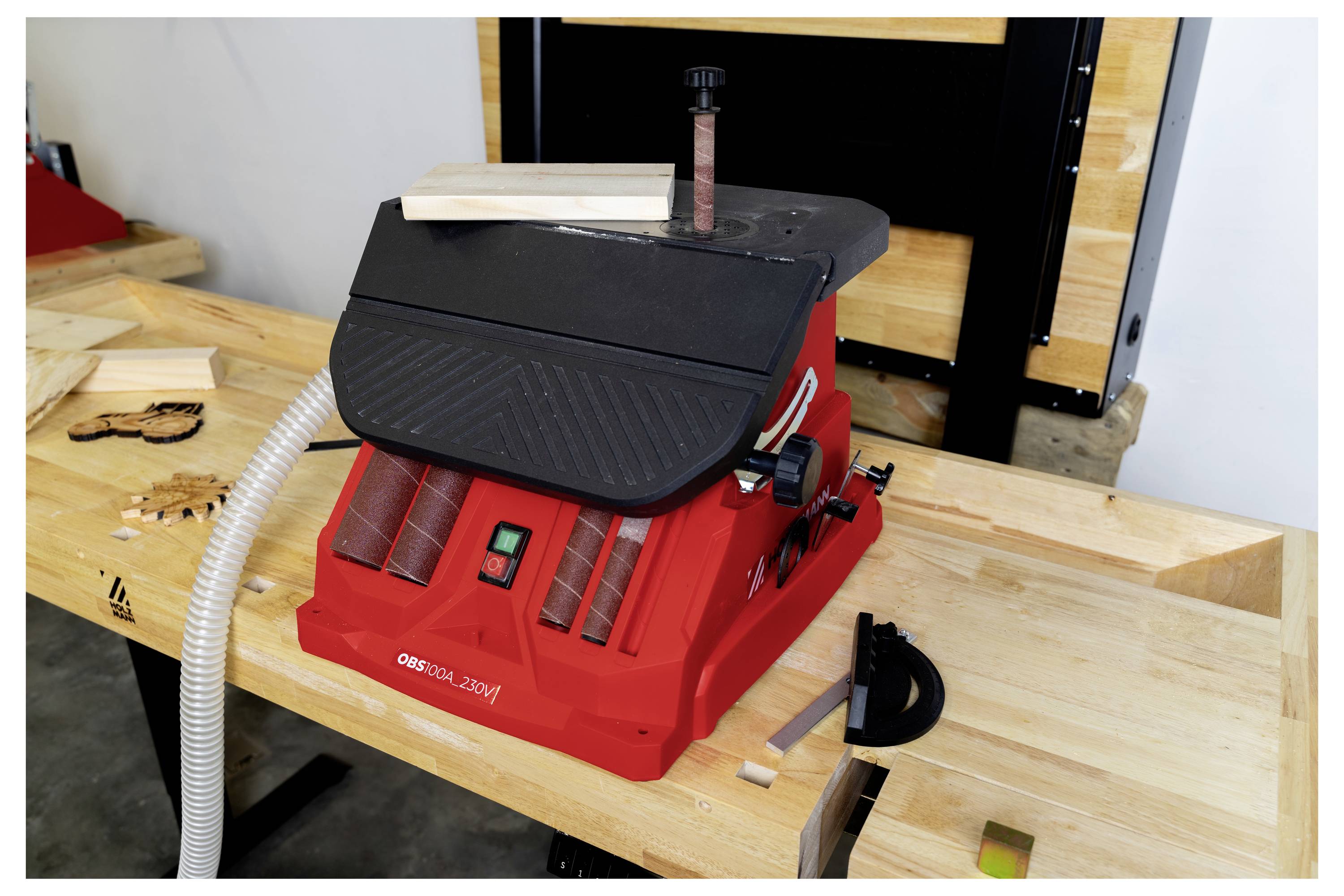 Eine rote Bandschleifmaschine auf einer Werkbank mit kleinen Holzstücken in der Nähe, was eine Holzbearbeitungseinrichtung andeutet.