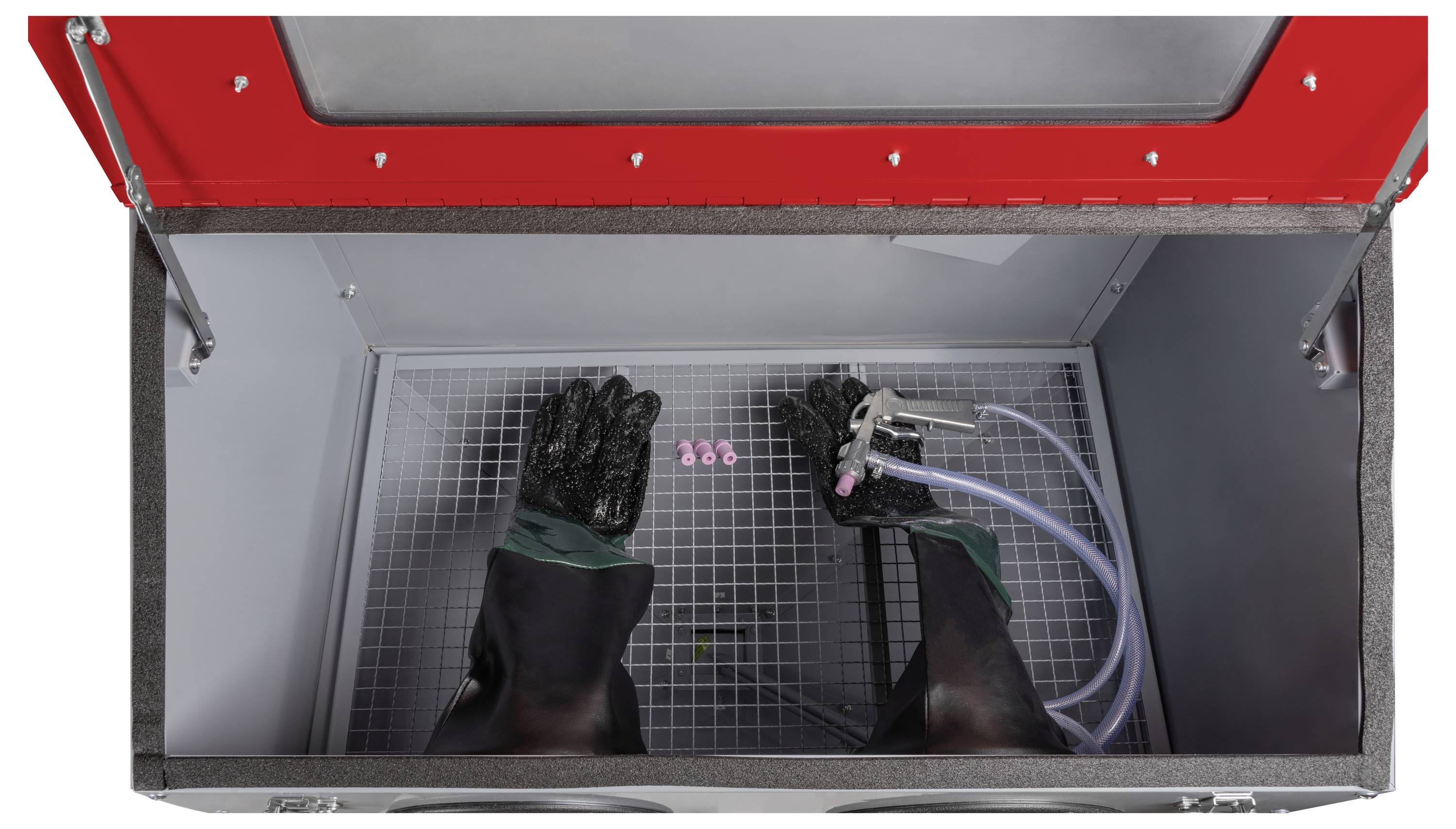 Draufsicht eines Sandstrahlschranks mit Handschuhen und Schlauch im Inneren, der den Arbeitsbereich zum sicheren Handhaben und Behandeln von Objekten zeigt.