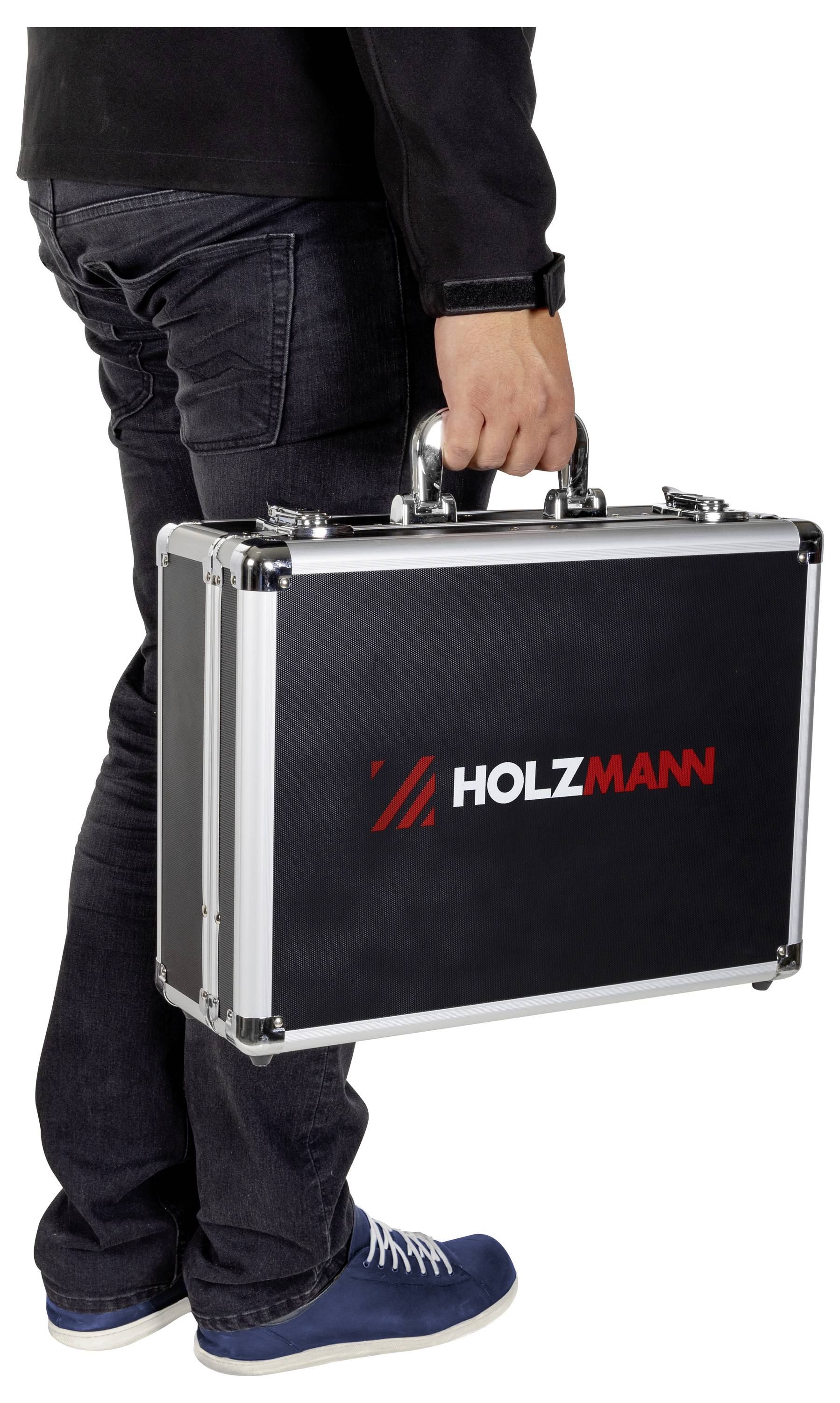 Eine Person, die einen schwarzen rechteckigen Aktenkoffer mit einem metallischen Griff trägt, auf dem der Markenname 'HOLZMANN' in roten und weißen Buchstaben angebracht ist.
