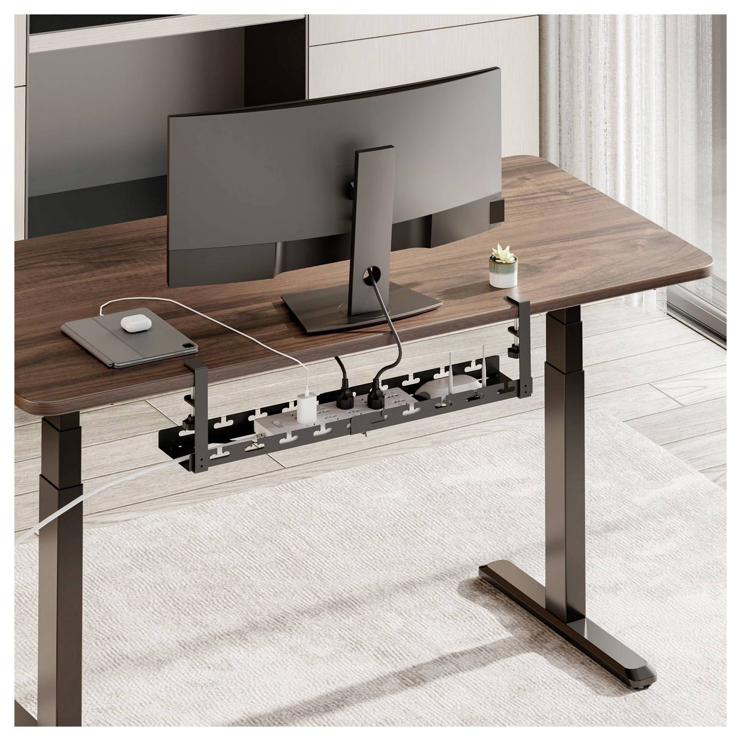 Ein modernes Büro mit einem Holzschreibtisch, auf dem ein schwarzer Monitor, ein Laptop und eine Mehrfachsteckdose platziert sind. Eine kleine Pflanze sorgt für einen Hauch von Grün.