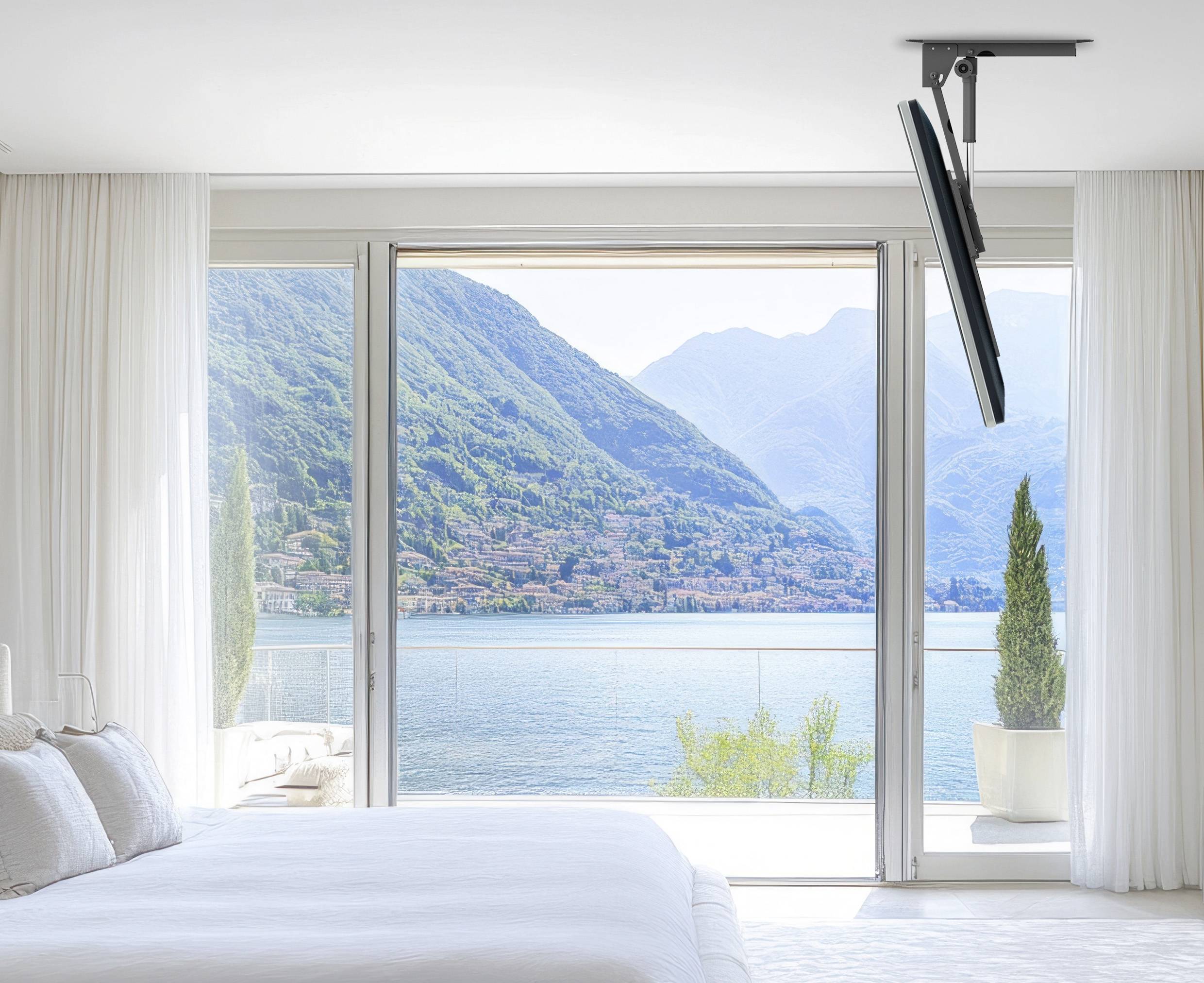 Ein ruhiges Schlafzimmer mit einem großen Fenster bietet einen atemberaubenden Ausblick auf einen friedlichen See, umgeben von üppig grünen Bergen unter einem klaren blauen Himmel.