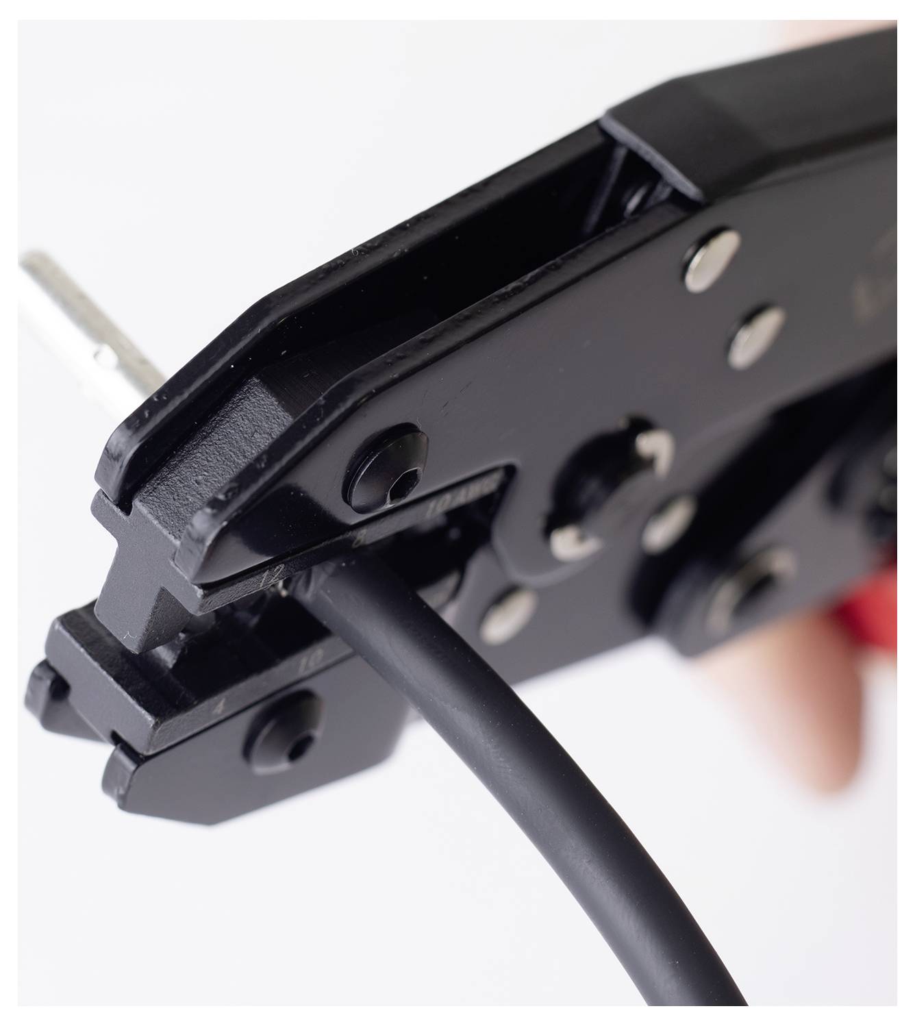 Eine Nahaufnahme einer schwarzen Drahtcrimpzange, die ein schwarzes Kabel umfasst, die zum Crimpen von elektrischen Leitungen verwendet wird, gehalten von einer Person im Hintergrund.