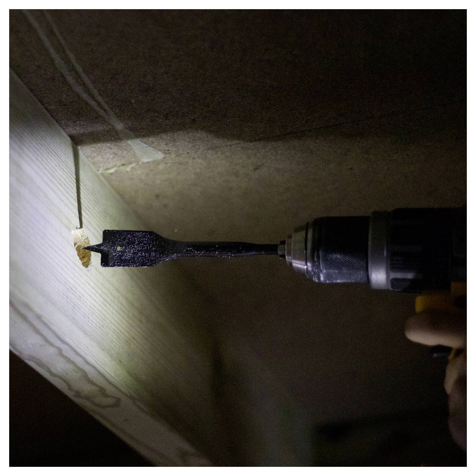 Eine Person verwendet eine Bohrmaschine, um ein Loch in ein Holzbrett zu bohren, mit einem Holzbohrer und etwas Licht, das den Arbeitsbereich beleuchtet.