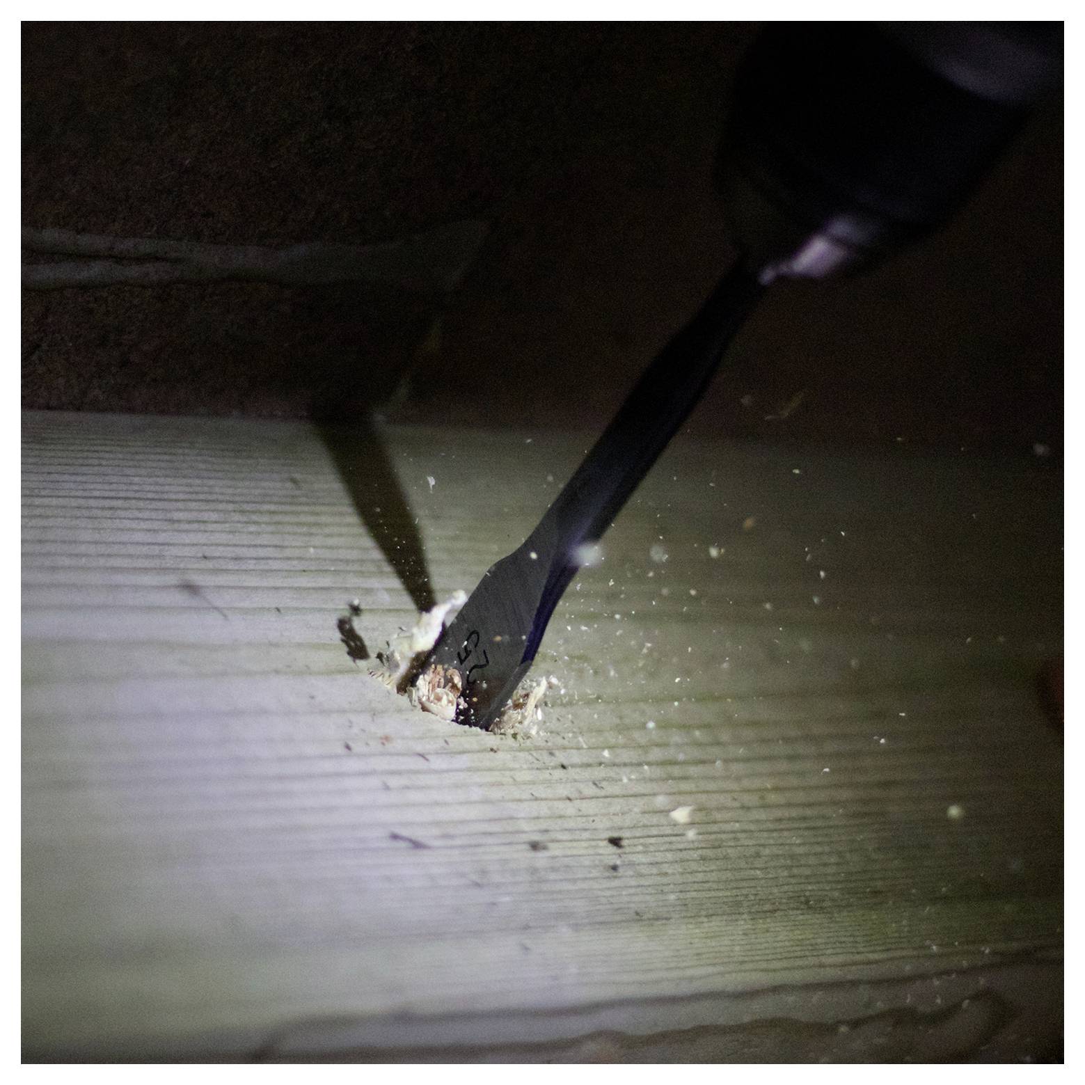 Eine Bohrmaschine, die ein Loch durch eine Holzoberfläche bohrt, mit Holzspänen, die verstreut sind und laufende Bau- oder Schreinerarbeiten andeuten.