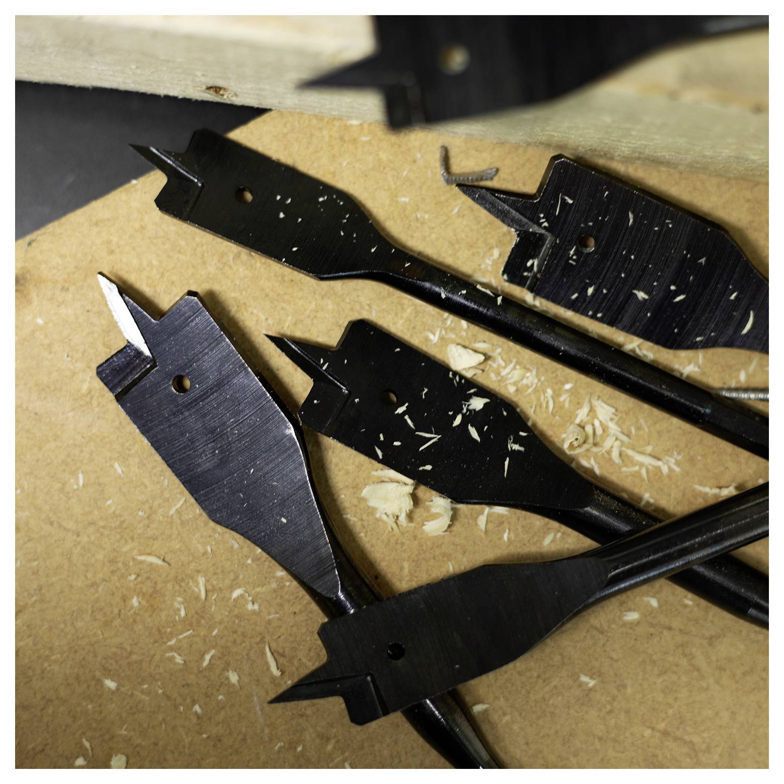Bohrer verstreut auf einer Holzoberfläche mit Holzspänen, was auf eine kürzlich durchgeführte oder laufende Schreinerarbeit hindeutet.