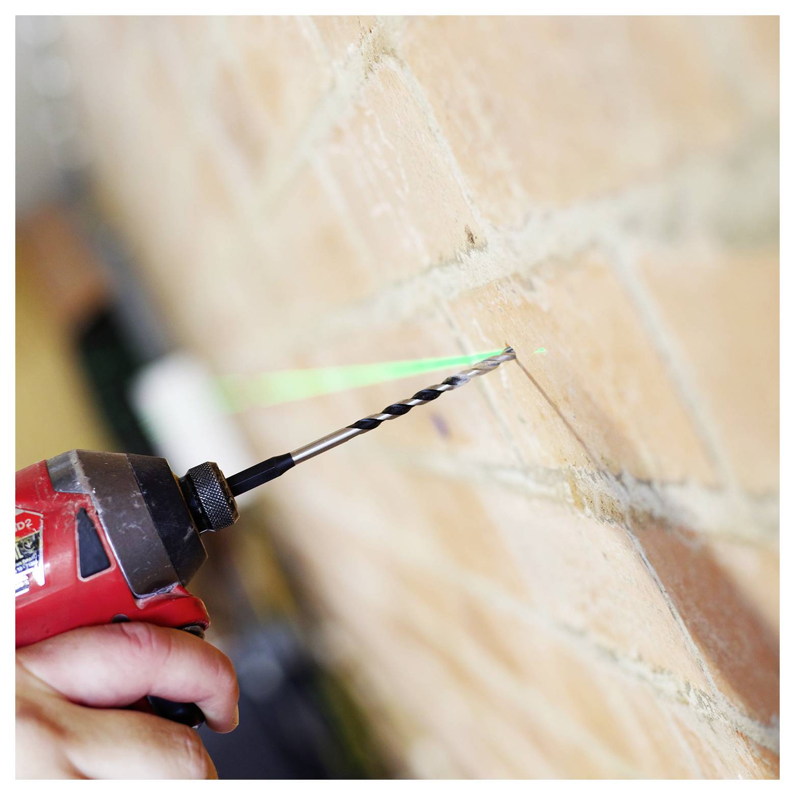 Eine Hand verwendet einen roten Akkuschrauber, um ein Loch in eine Ziegelwand zu bohren, geführt von einem grünen Laser für Präzision.