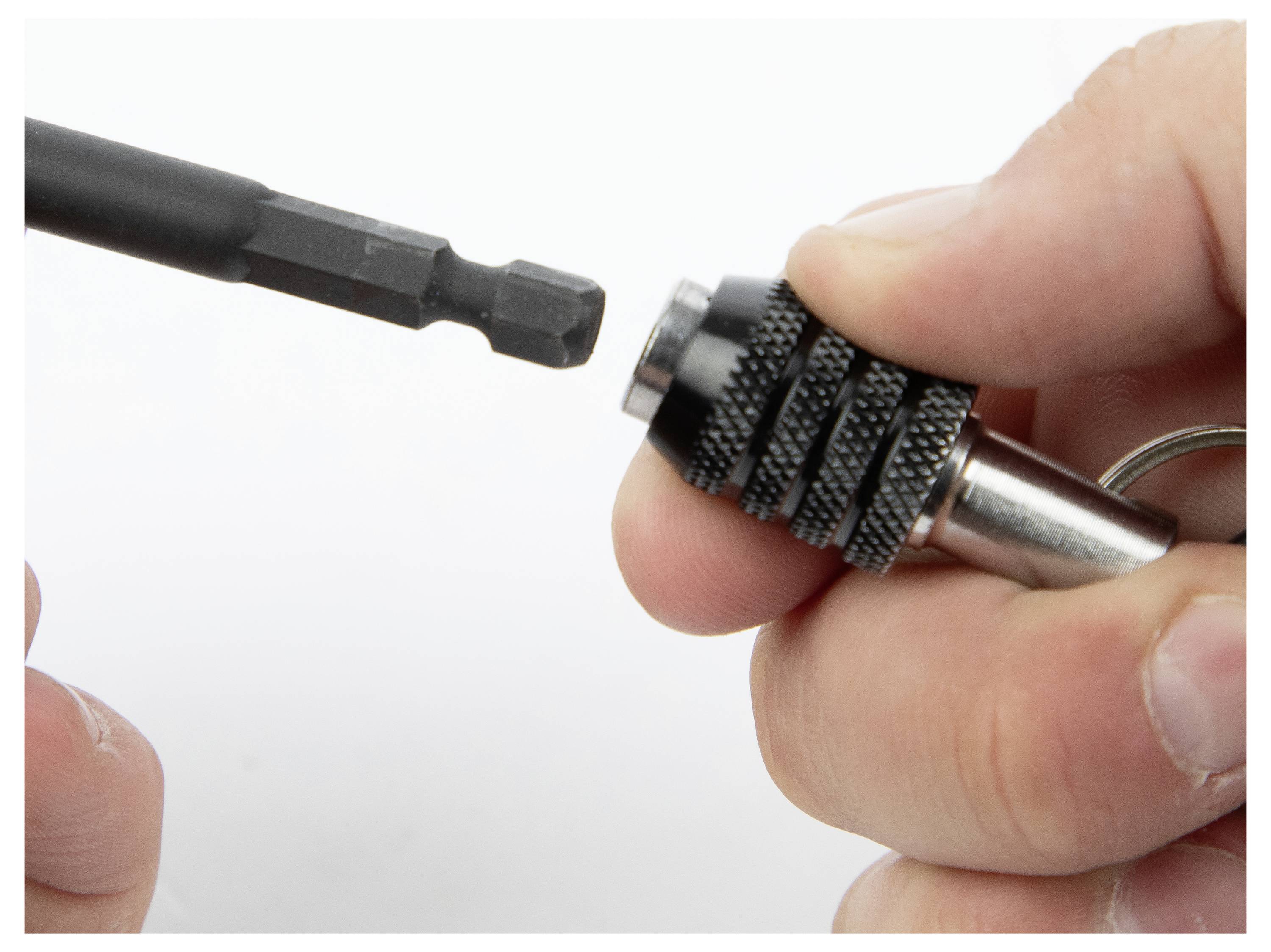 Eine Hand, die einen schwarzen Metallbit hält, neben einer Nahaufnahme einer anderen Hand, die einen schwarz-silbernen Bohrfutterkopf hält, bereit zur Einsetzung.