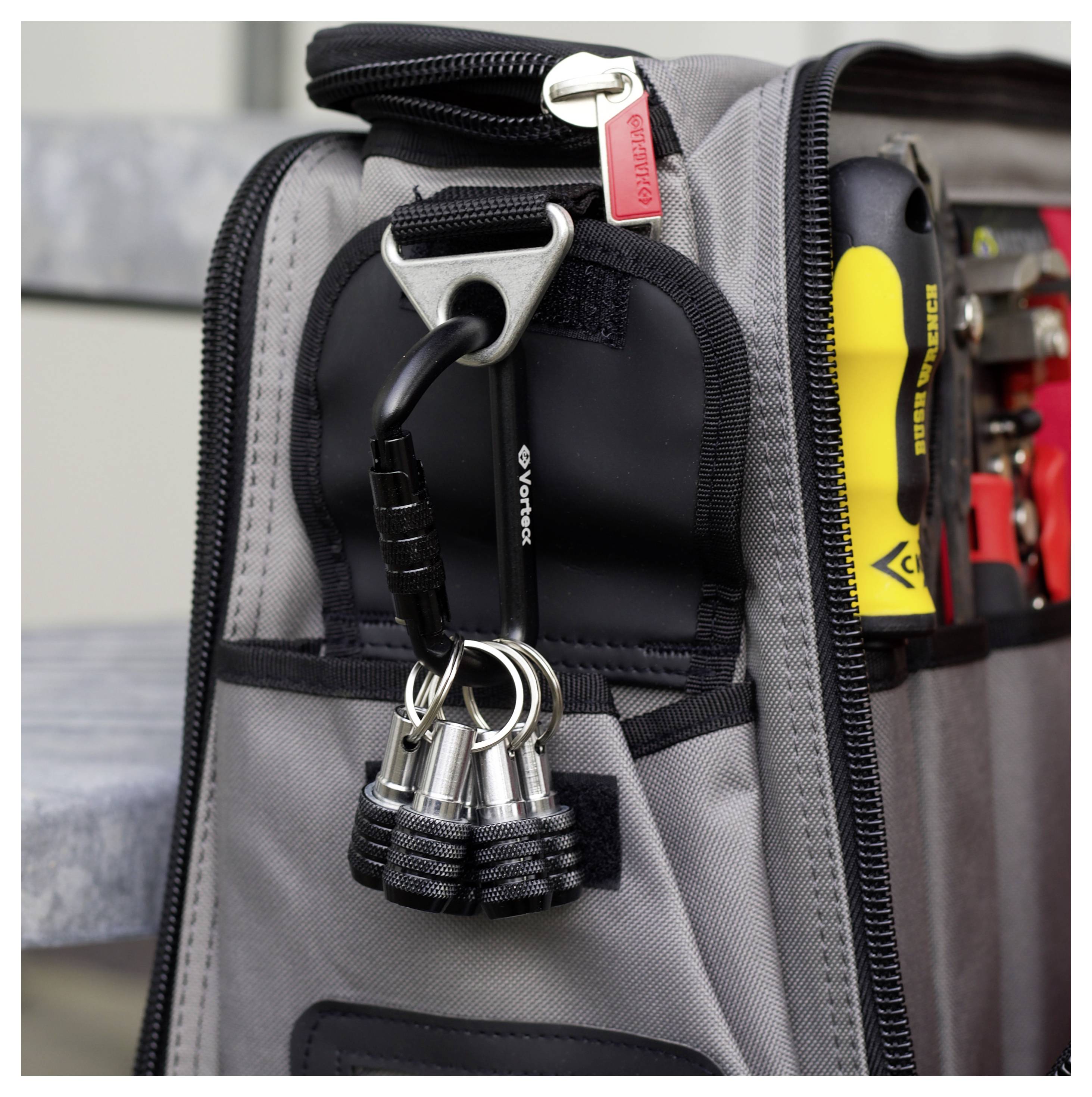 Eine graue Werkzeugtasche mit verschiedenen Werkzeugen in Fächern, darunter ein gelber Schraubendreher und ein schwarzer Schraubenschlüssel, hängt auf einem Steinvorsprung.