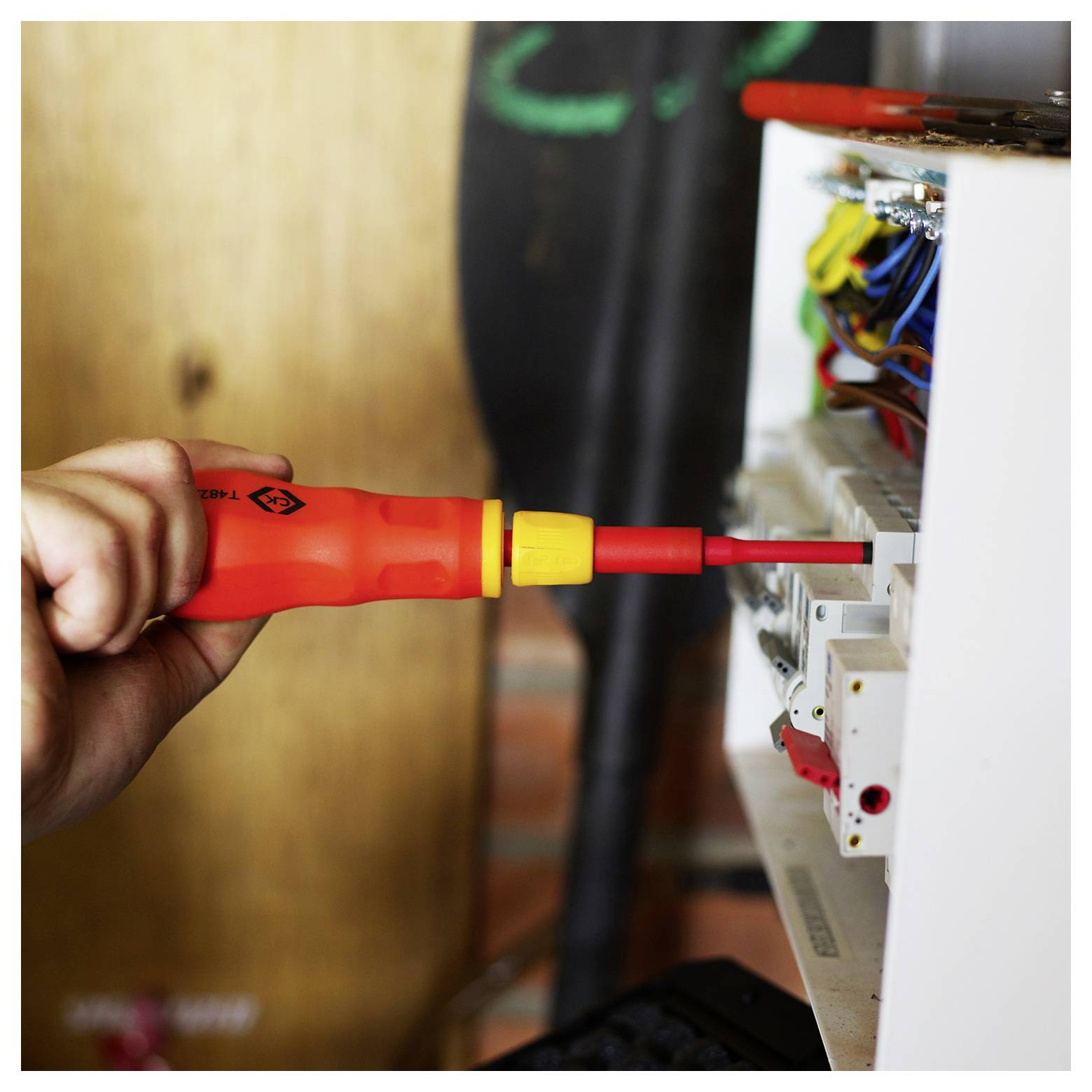 Eine Person verwendet einen isolierten Schraubendreher, um an einer Sicherungsbox zu arbeiten und sich dabei auf die Verkabelung zu konzentrieren. Die Szene hebt elektrische Arbeiten und Sicherheitswerkzeuge hervor.