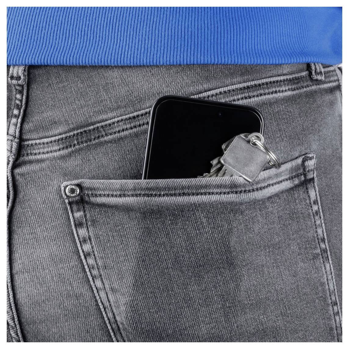 Ein Smartphone und Schlüssel, die aus der Gesäßtasche einer grauen Jeans gegen einen blauen Hintergrund hervorschauen.