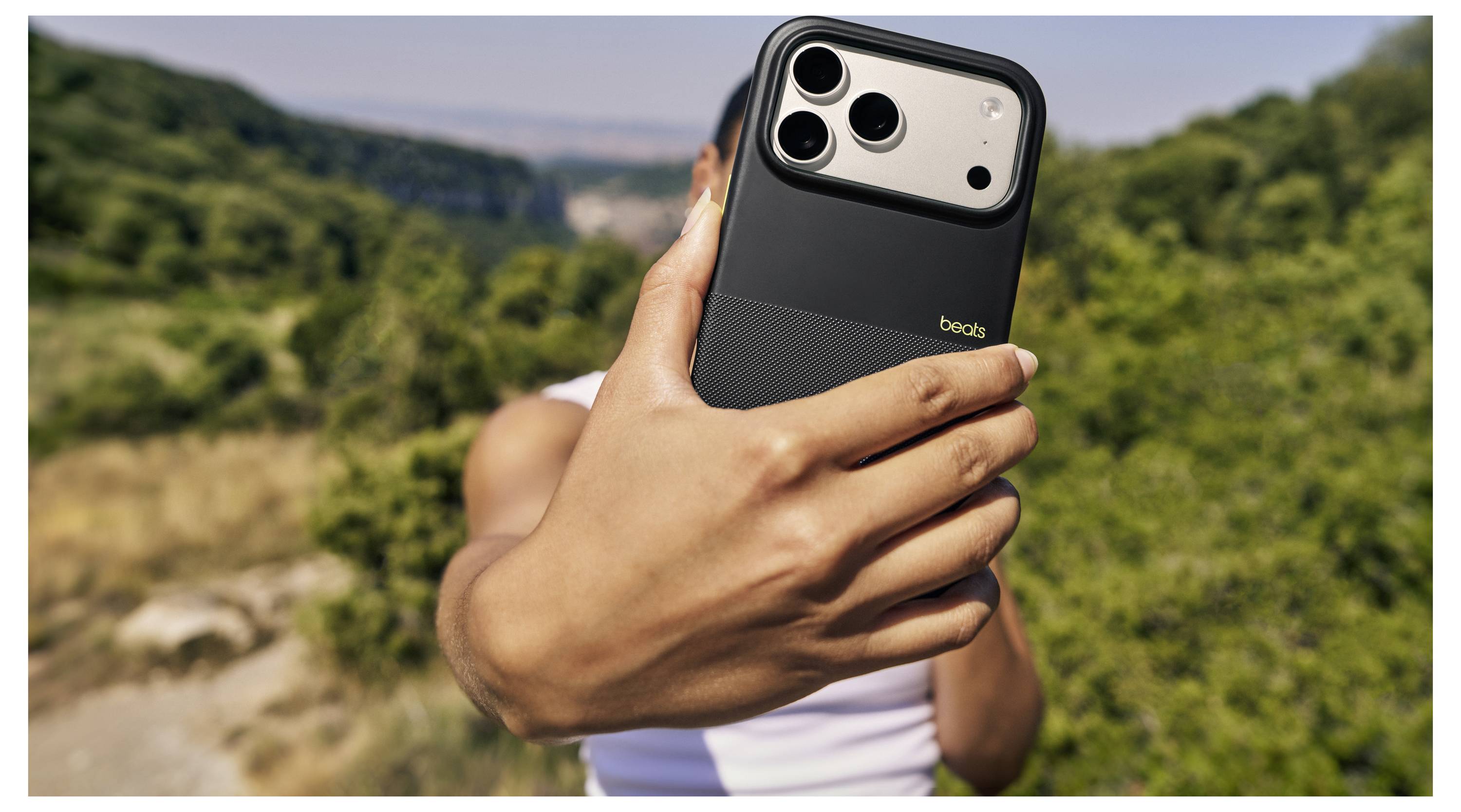 Eine Person hält ein Smartphone mit Fokus auf die Rückkamera in einer Outdoor-Landschaft mit grüner Umgebung.