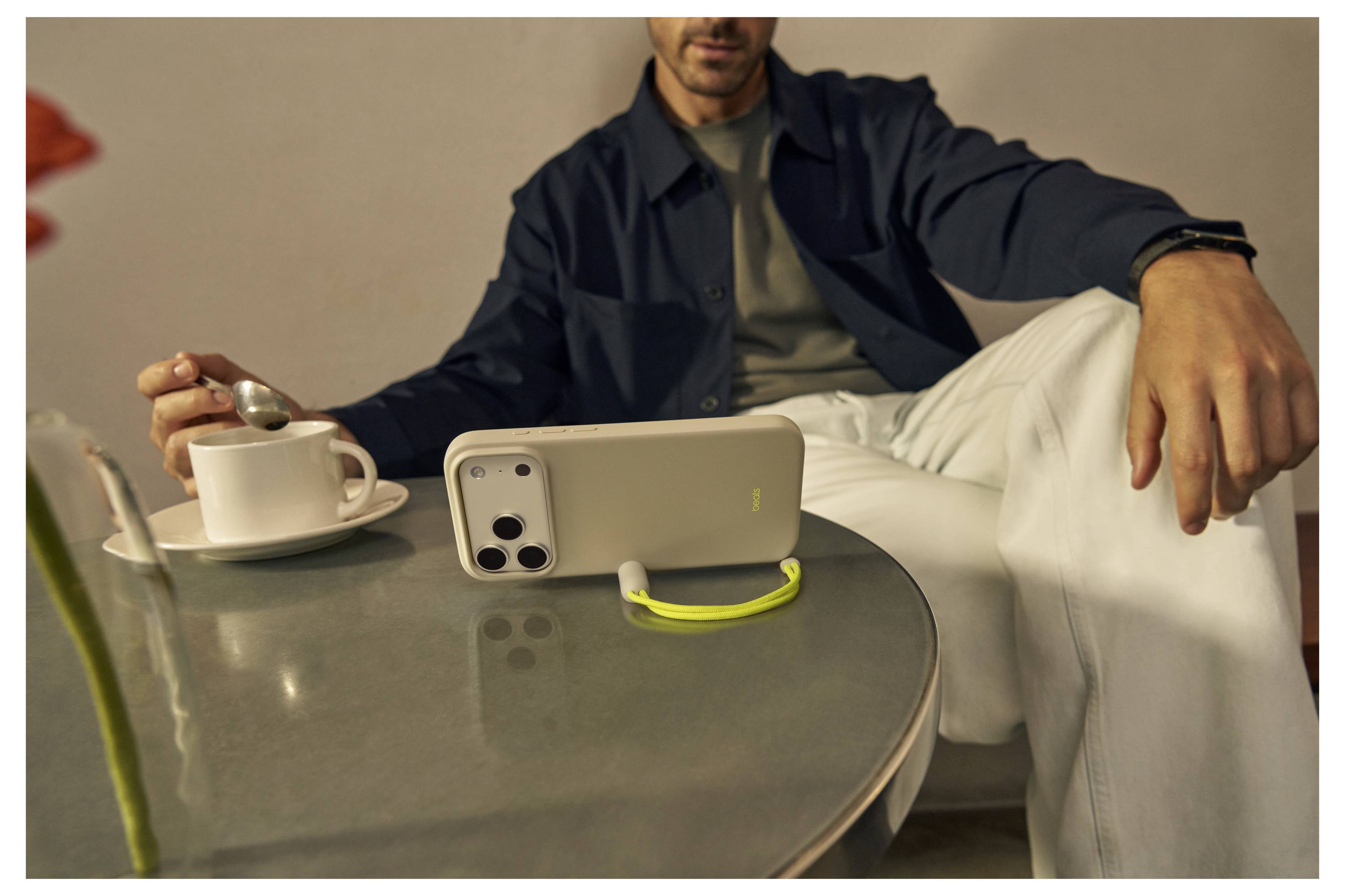 Eine Person sitzt an einem Tisch mit einem Smartphone, das auf der Seite steht, neben einer Tasse, während sie sich anschickt, ihr Getränk zu rühren.