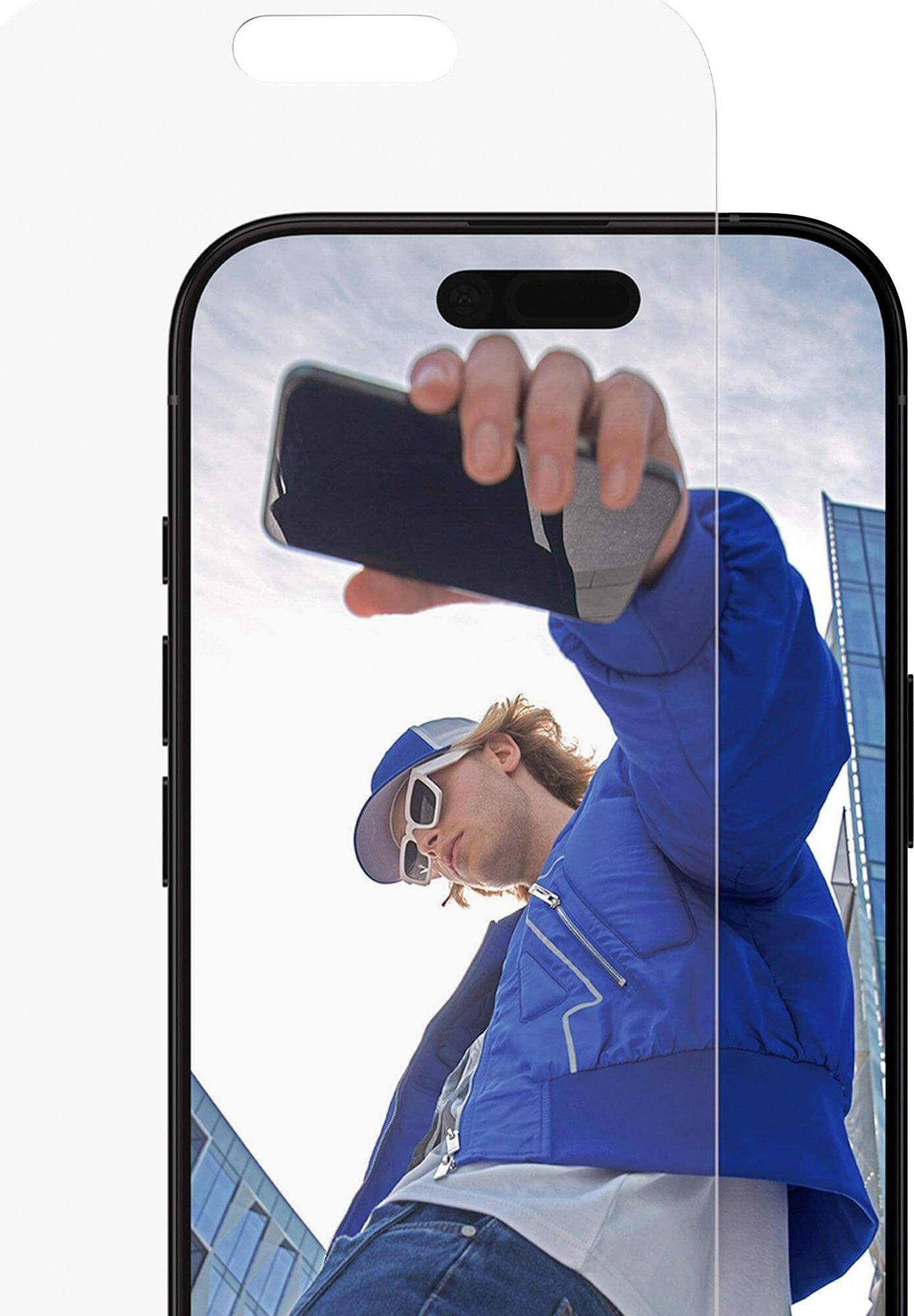 Eine Person mit blauer Jacke und Sonnenbrille macht mit einem Smartphone ein Selfie, während sie vor modernen Glasgebäuden unter einem klaren Himmel steht.