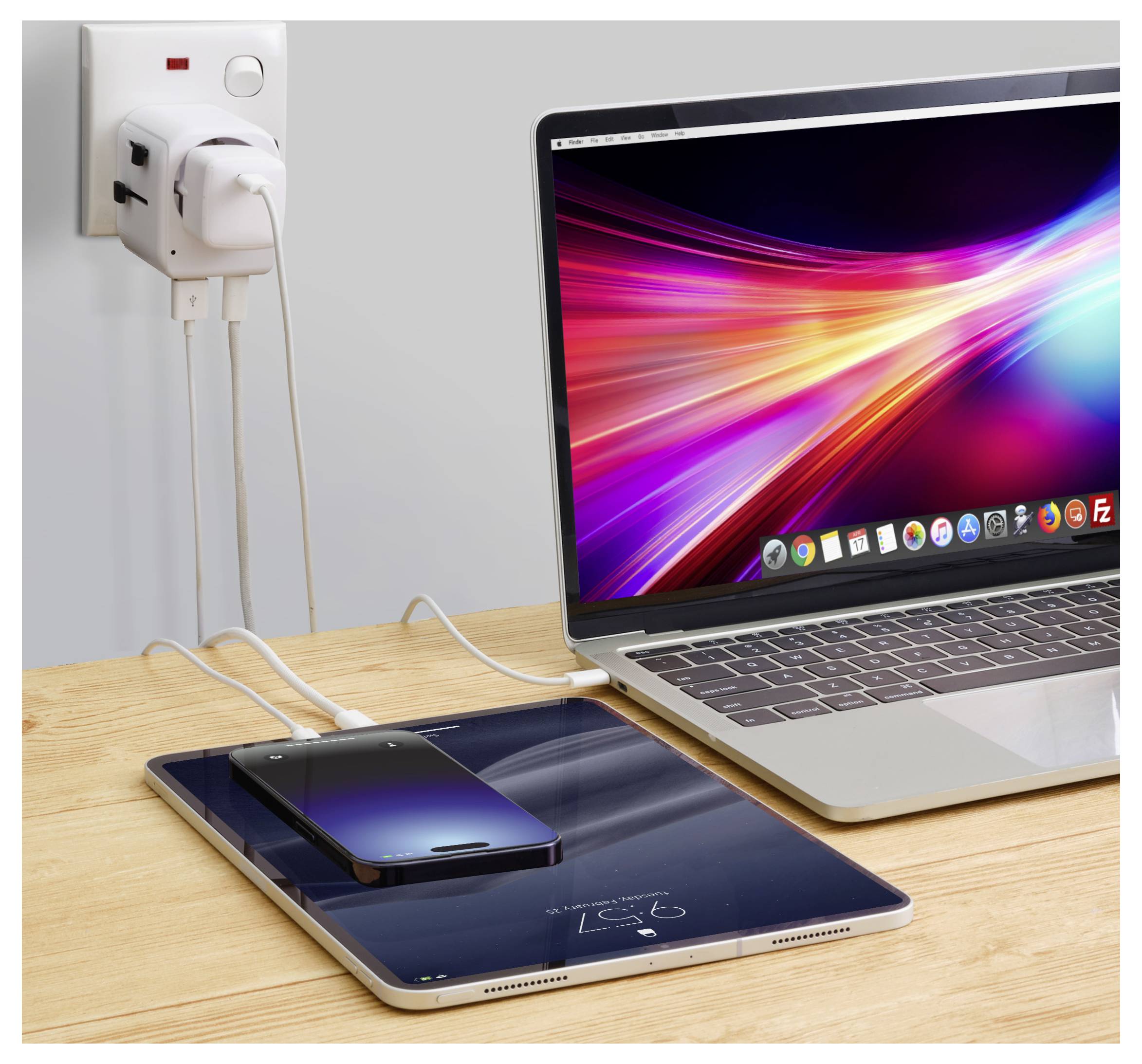 Ein Laptop mit einem leuchtenden Bildschirm, ein Smartphone und ein Tablet laden auf einem Holzschreibtisch, die an eine Steckdose angeschlossen sind.