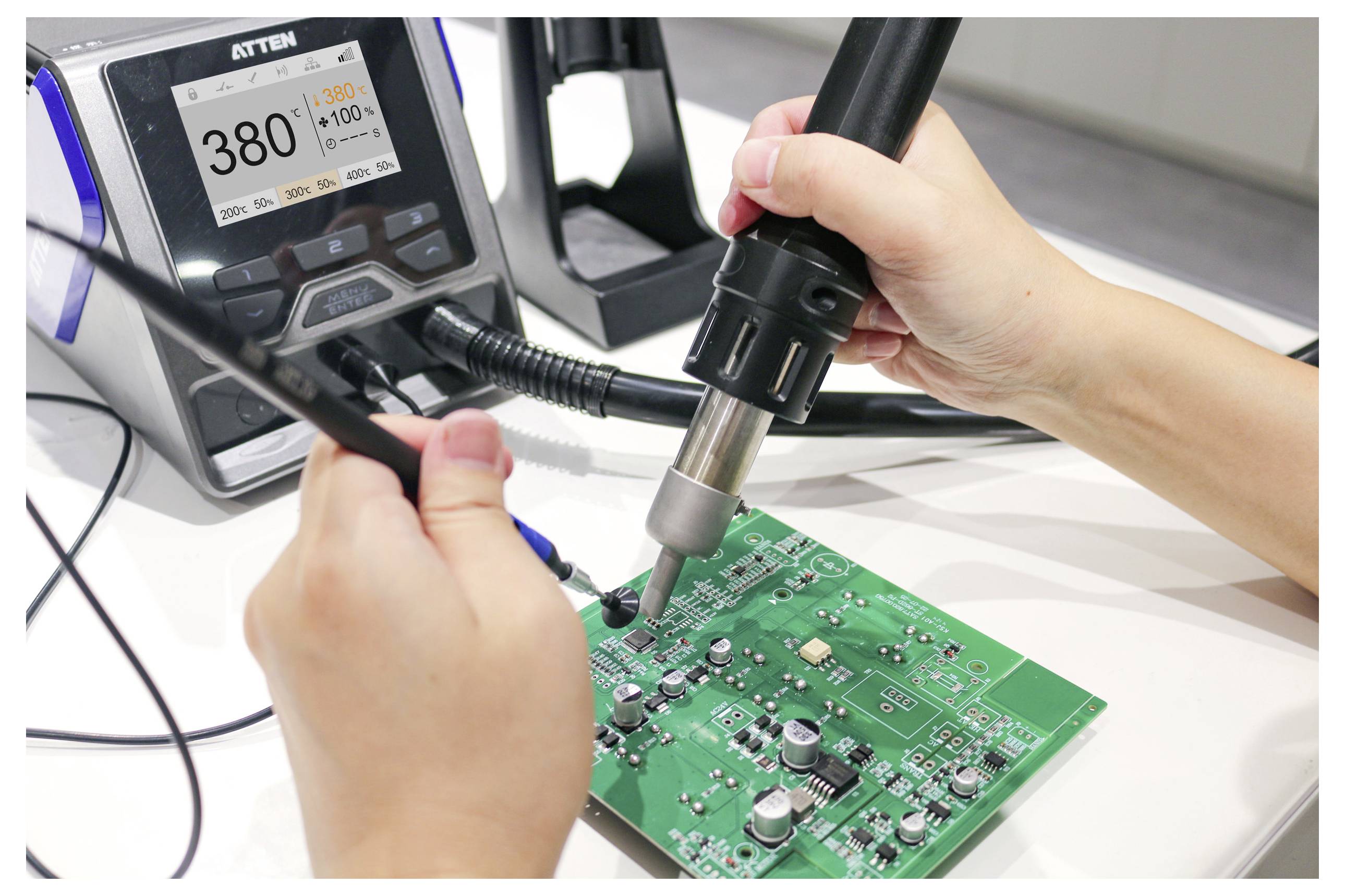Eine Person verwendet eine Heißluftpistole und eine Pinzette, um an einer grünen Leiterplatte zu arbeiten. Eine digitale Temperaturanzeige zeigt '380°C' neben dem Arbeitsbereich.