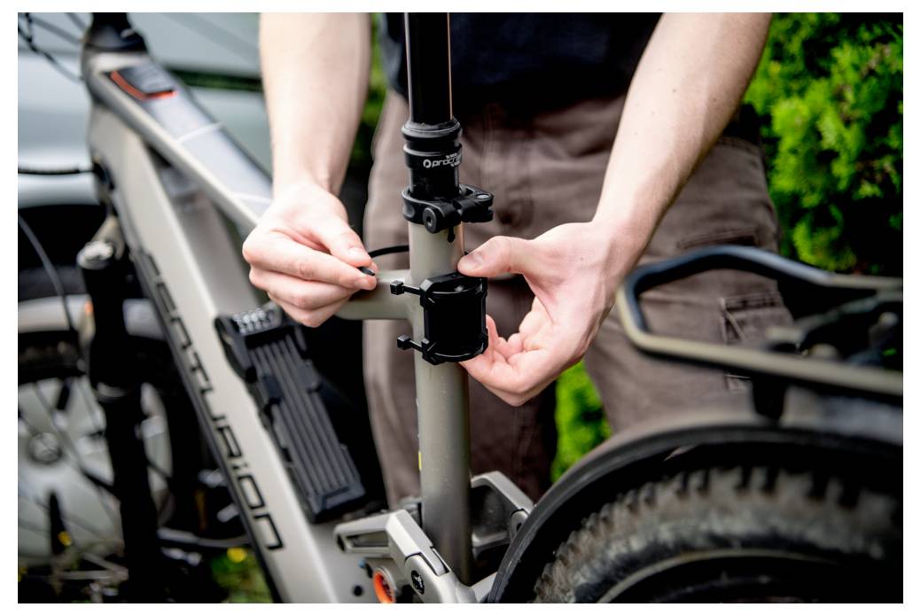 Eine Person, die die Sattelklemme eines grauen Fahrrads einstellt. Hände, die einen Bolzen an der Klemme festziehen, was auf Wartung oder Vorbereitung für eine Fahrt hinweist.