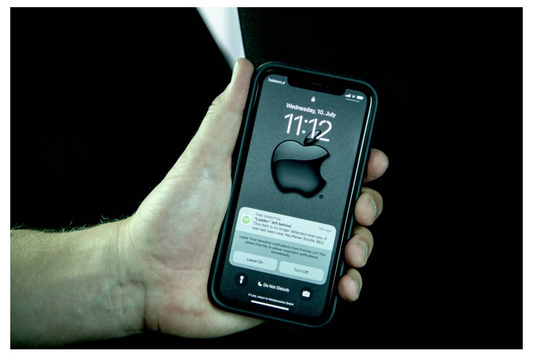 Eine Hand hält ein Smartphone mit einem Sperrbildschirm, auf dem ein großes Apple-Logo, eine Uhrzeit von '11:12' und Benachrichtigungen zu sehen sind.