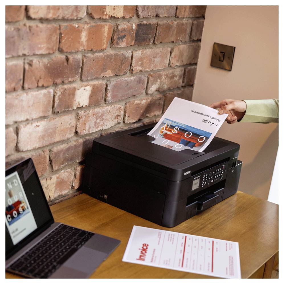 Eine Person legt ein Papier von 'Office Solutions' in einen schwarzen Drucker auf einem Holztisch, während ein Laptop ein ähnliches Dokument anzeigt.