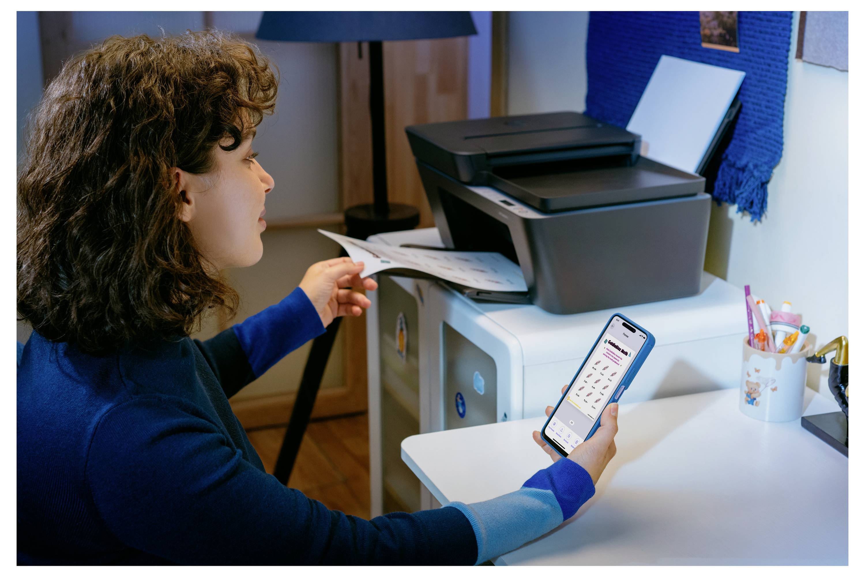 Frau nutzt ein Smartphone, um ein Dokument neben einem Desktop-Drucker auf einem Schreibtisch im Homeoffice zu scannen oder zu drucken.