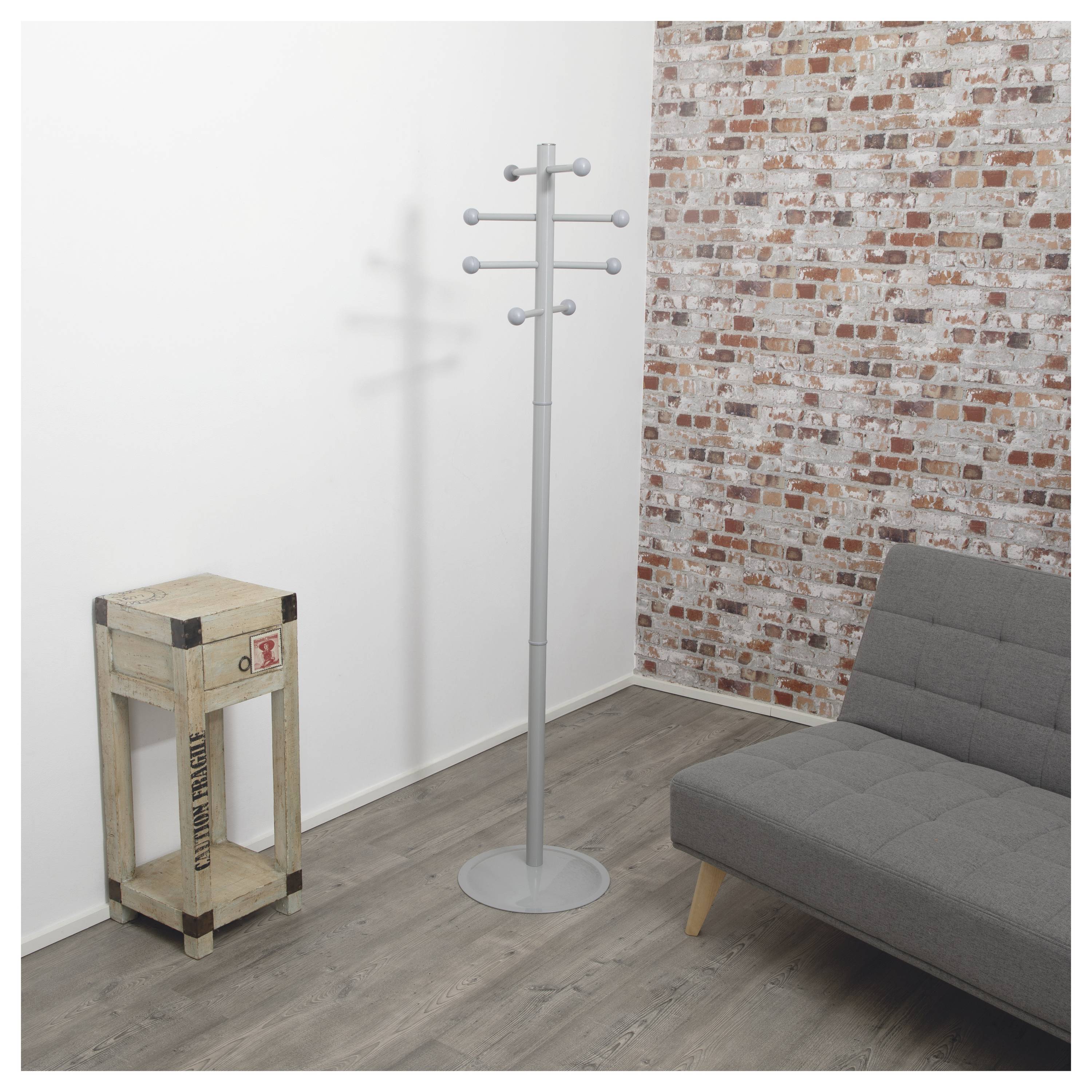 Ein minimalistisches Zimmer mit einer Garderobe, einer Holzkiste und einem grauen Sofa an einer Ziegelwand. Die Umgebung deutet auf eine moderne, industrielle Einrichtung hin.