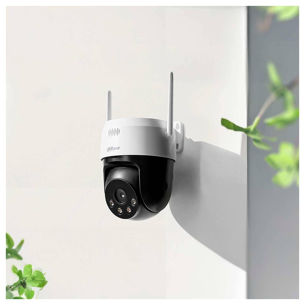 Eine wandmontierte Sicherheitskamera mit Antennen und Infrarotlichtern. Sie ist im Freien positioniert, umgeben von verschwommener Vegetation.