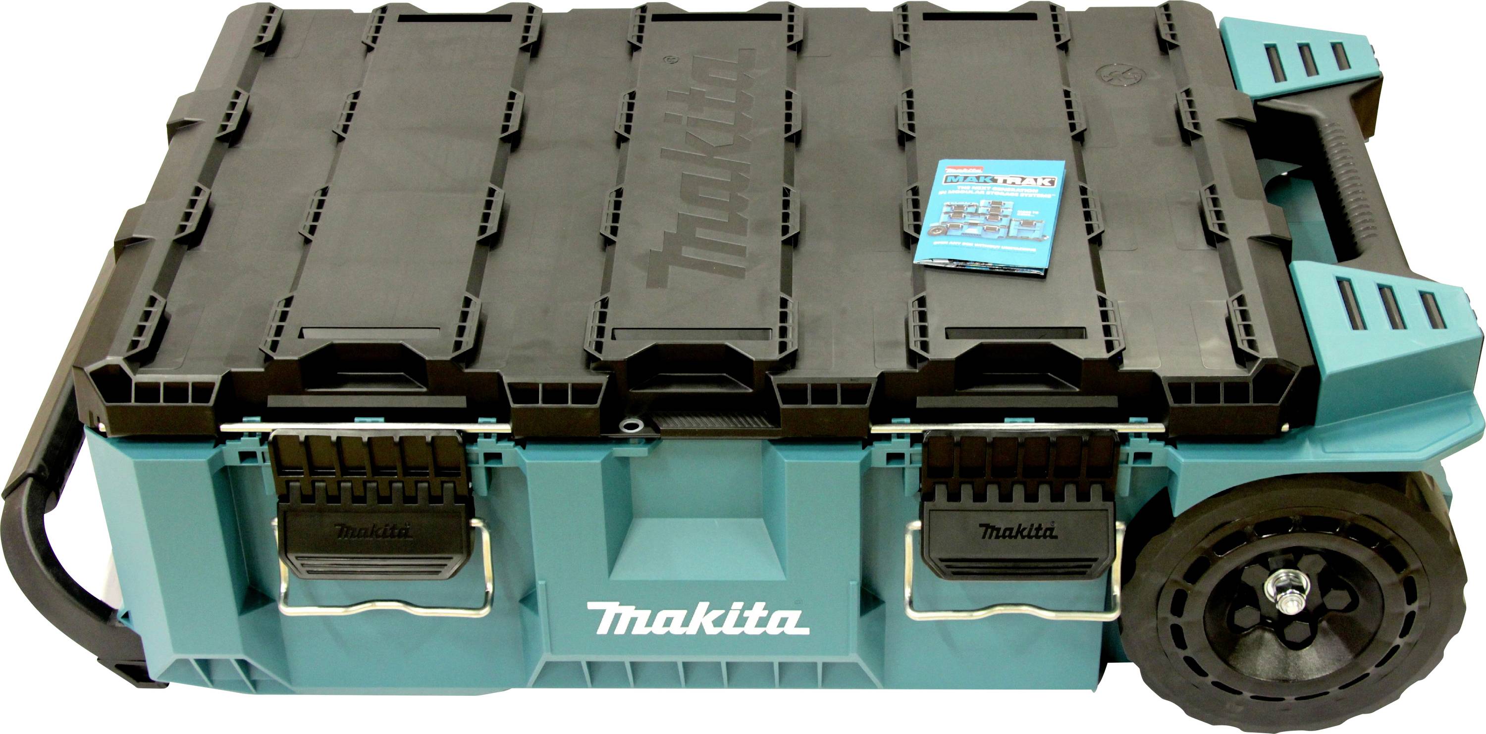 Makita Werkzeugaufbewahrungsbox mit schwarzem Deckel, zwei vorderen Verschlüssen, Rädern auf der rechten Seite und einem Griff. Beinhaltet ein kleines blaues Handbuch auf der Oberseite.