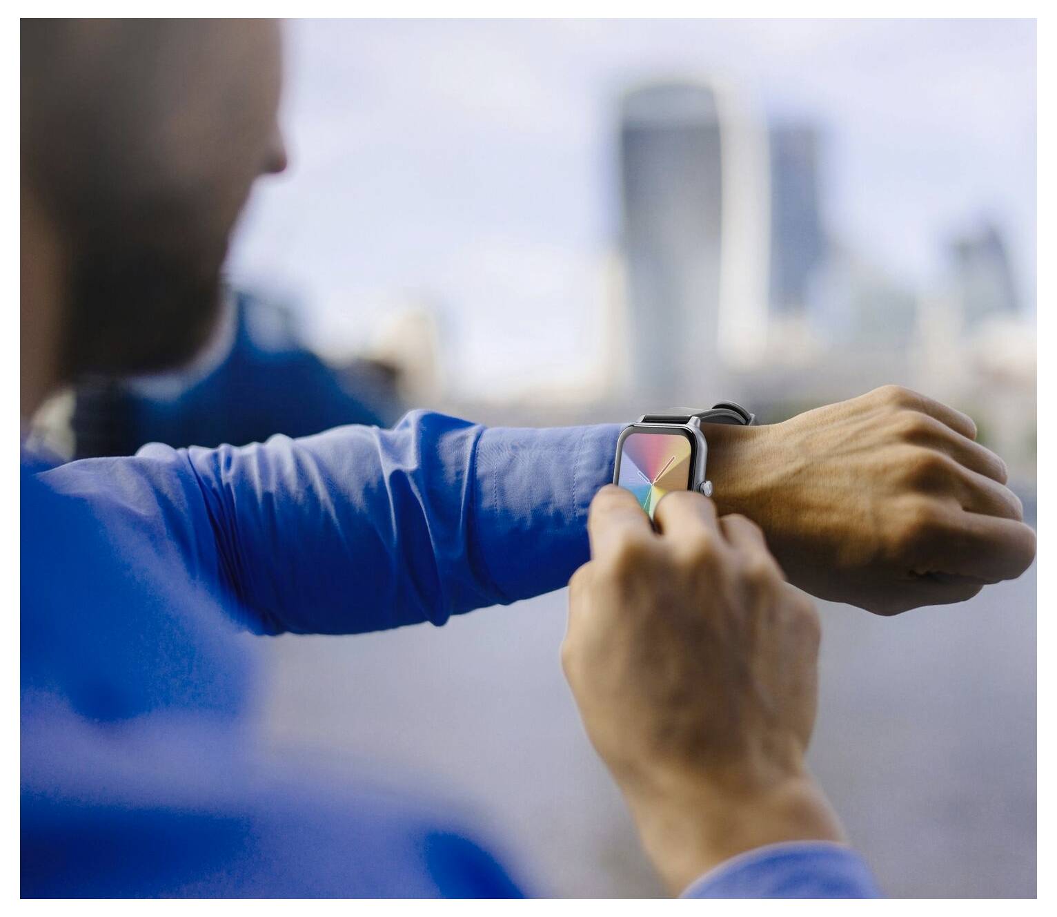 Eine Person in einem blauen Hemd interagiert mit einer Smartwatch, die bunte Symbole anzeigt, während ein unscharfer städtischer Horizont im Hintergrund zu sehen ist.