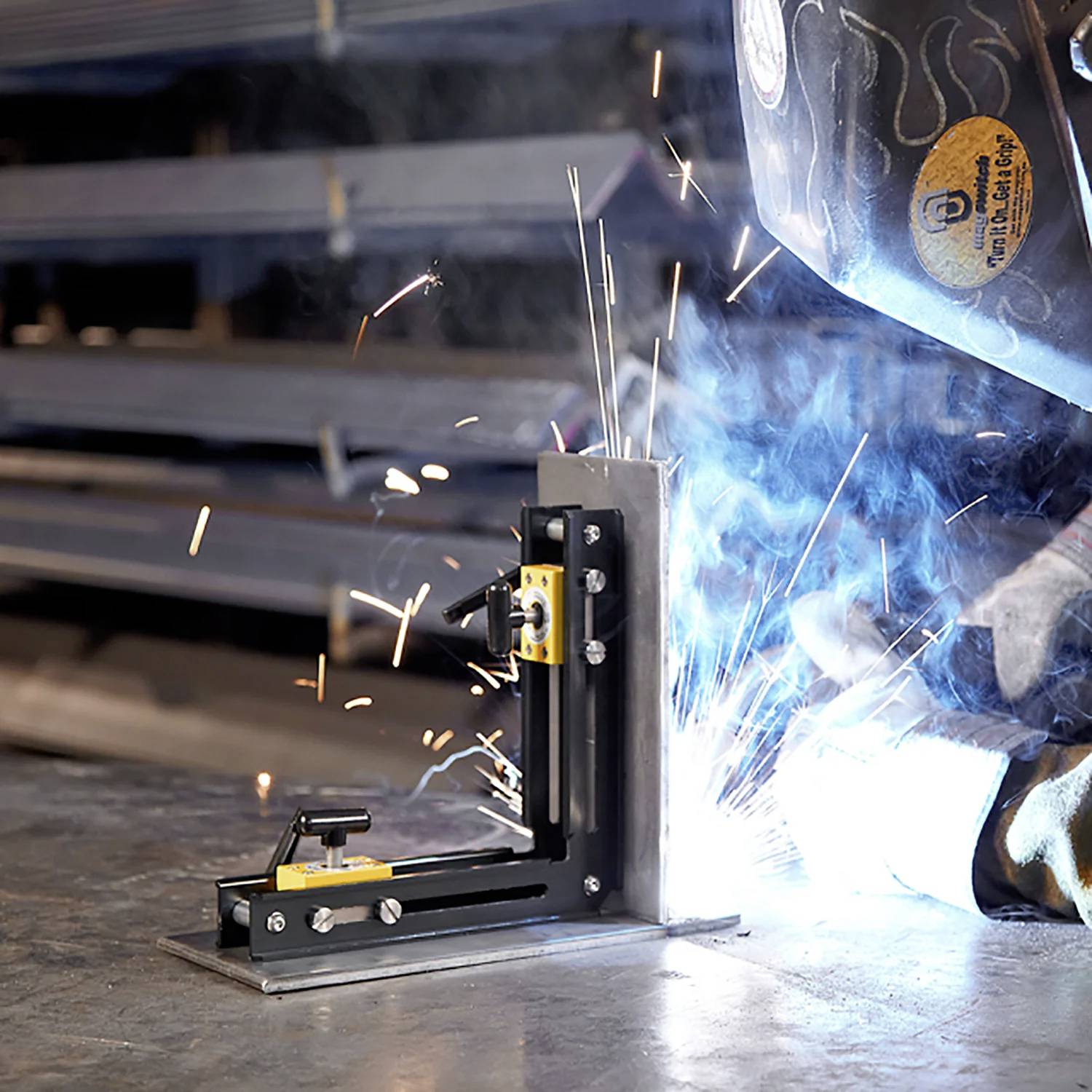 Eine Person schweißt Metall in einer Werkstatt, wobei Funken umherfliegen. Der Arbeitsbereich ist mit Sicherheitsausrüstung, einschließlich eines Helms, ausgestattet.