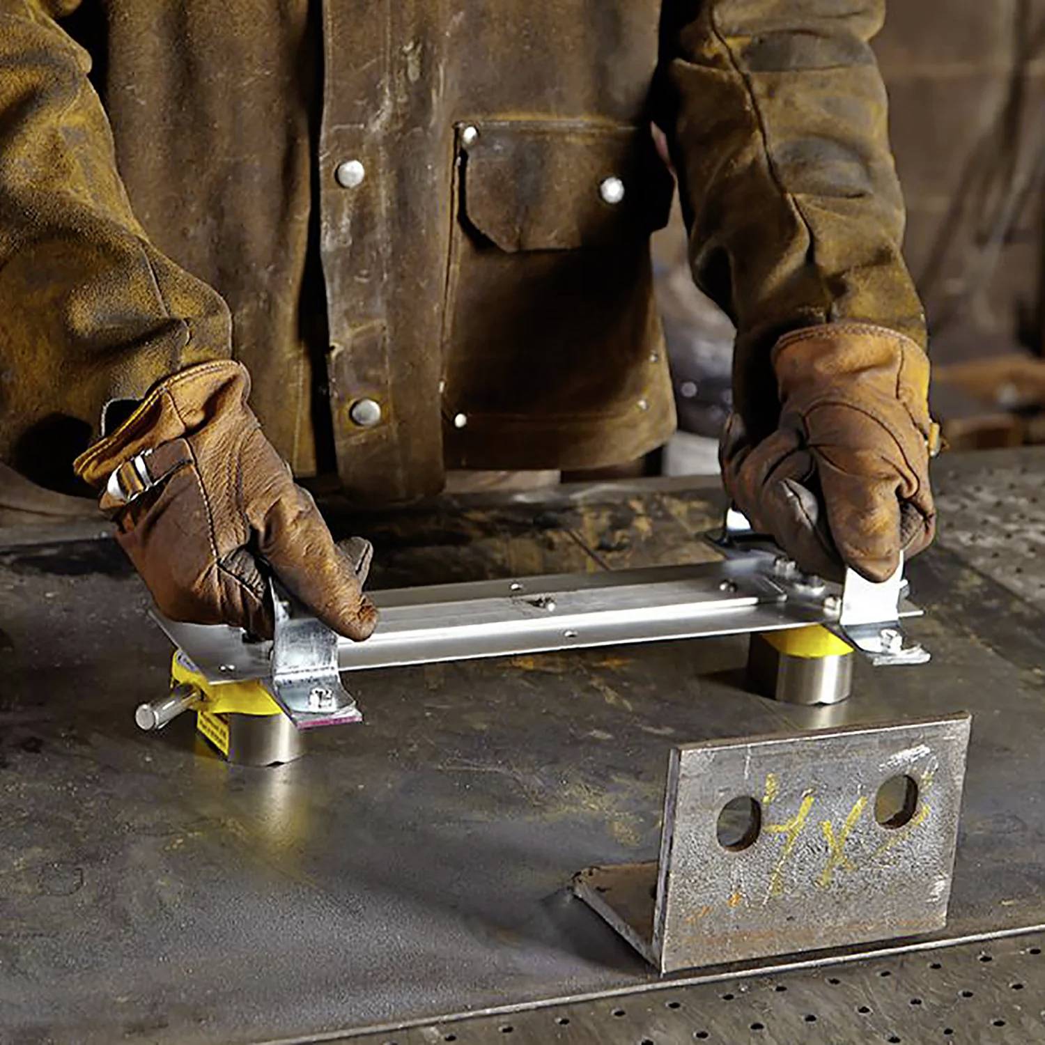 Eine Person mit Handschuhen demonstriert das Befestigen eines Metallstücks an einem Magnethalter auf einem Werkstatttisch, umgeben von Werkzeugen und Metallteilen.