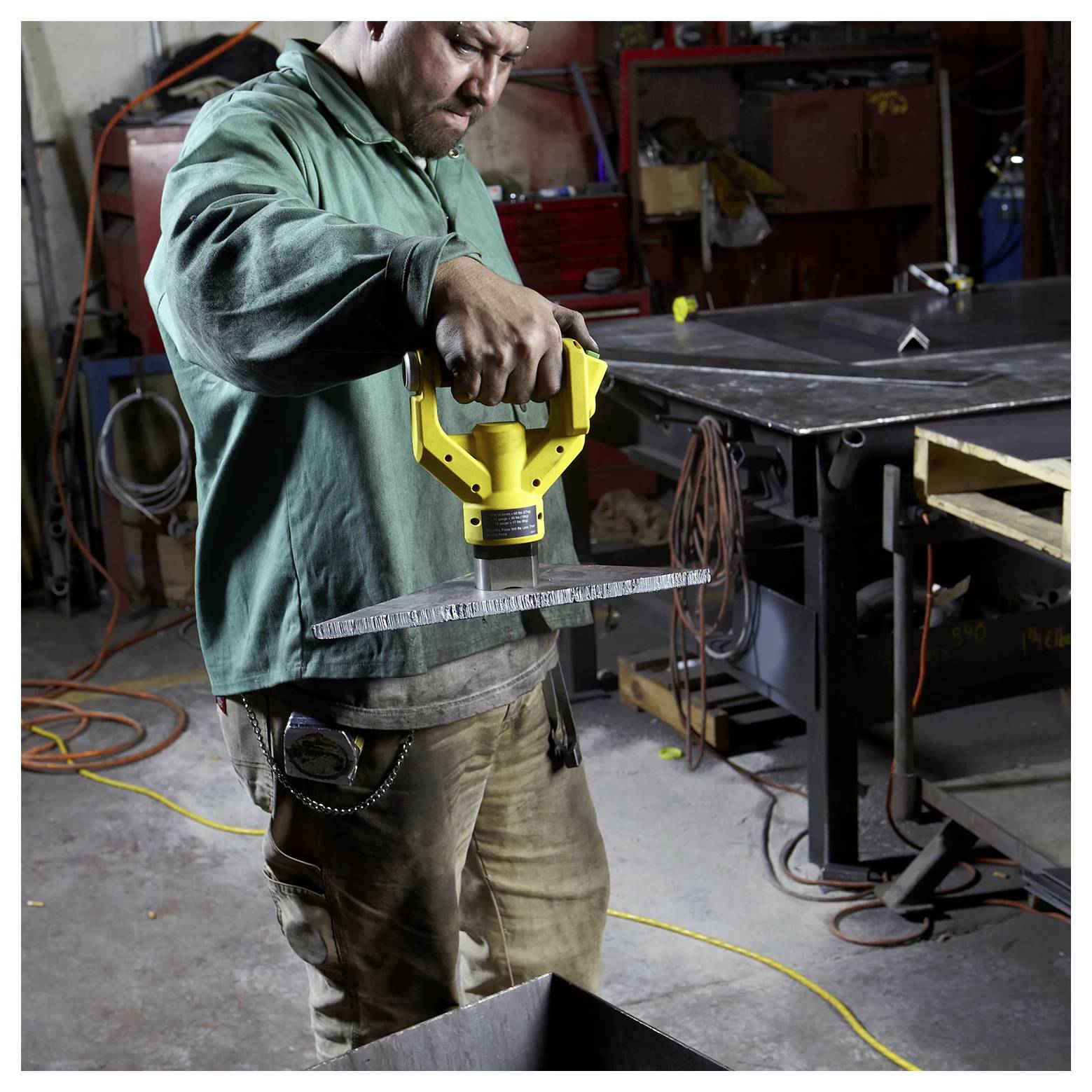 Eine Person in einer Werkstatt verwendet ein Messwerkzeug, um die Abmessungen eines Materialstücks zu überprüfen, umgeben von Werkzeugen und Ausrüstung.