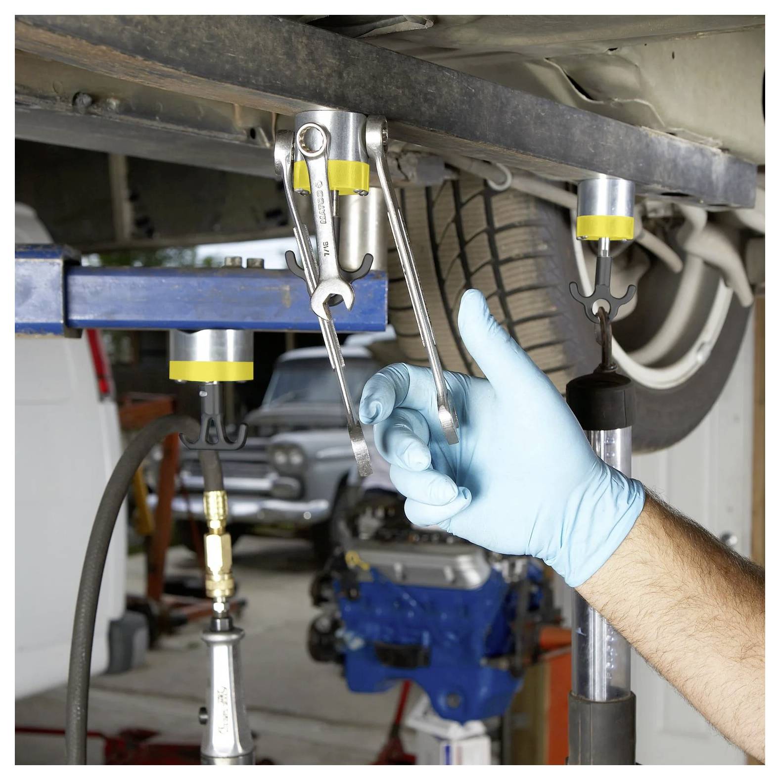 Eine Person mit einem blauen Handschuh verwendet einen Schraubenschlüssel, um eine Schraube an einem Autoreifen zu befestigen, der mit Sicherheitsabstützungen in einer Autowerkstatt gesichert ist.