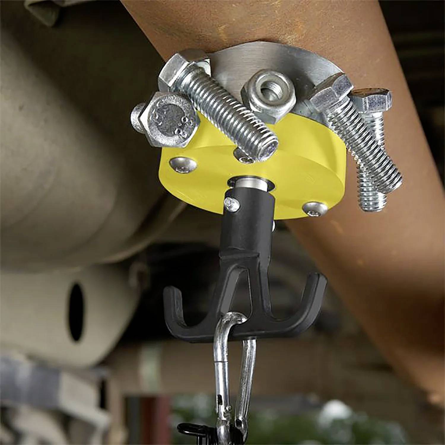 Ein Werkzeug ist mit einer gelben Klemme, die vier Metallschrauben enthält, an einem hängenden Auspuffrohr befestigt und stützt das Rohr während der Reparaturarbeiten.
