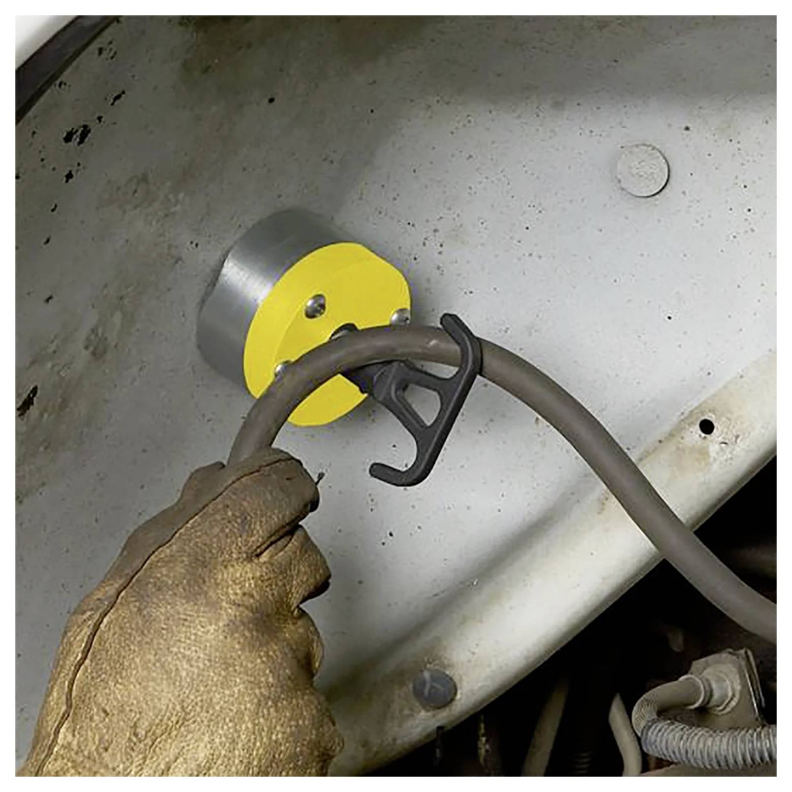 Eine Hand in einem Handschuh zieht einen Metallkabelhaken von einem Magnethalter auf einer weißen Metalloberfläche.