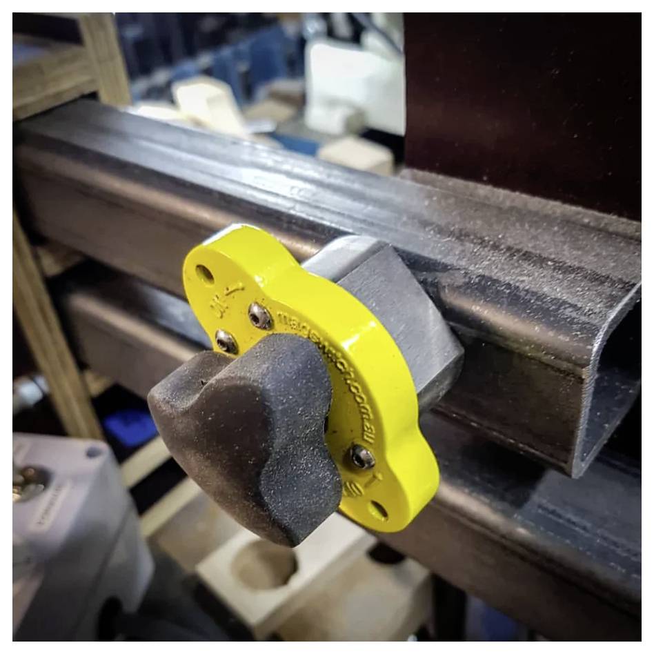 Ein gelb-schwarzer Knopf, der an einer Metallschiene einer Maschine befestigt ist und zum Einstellen oder Sichern des Mechanismus verwendet wird.