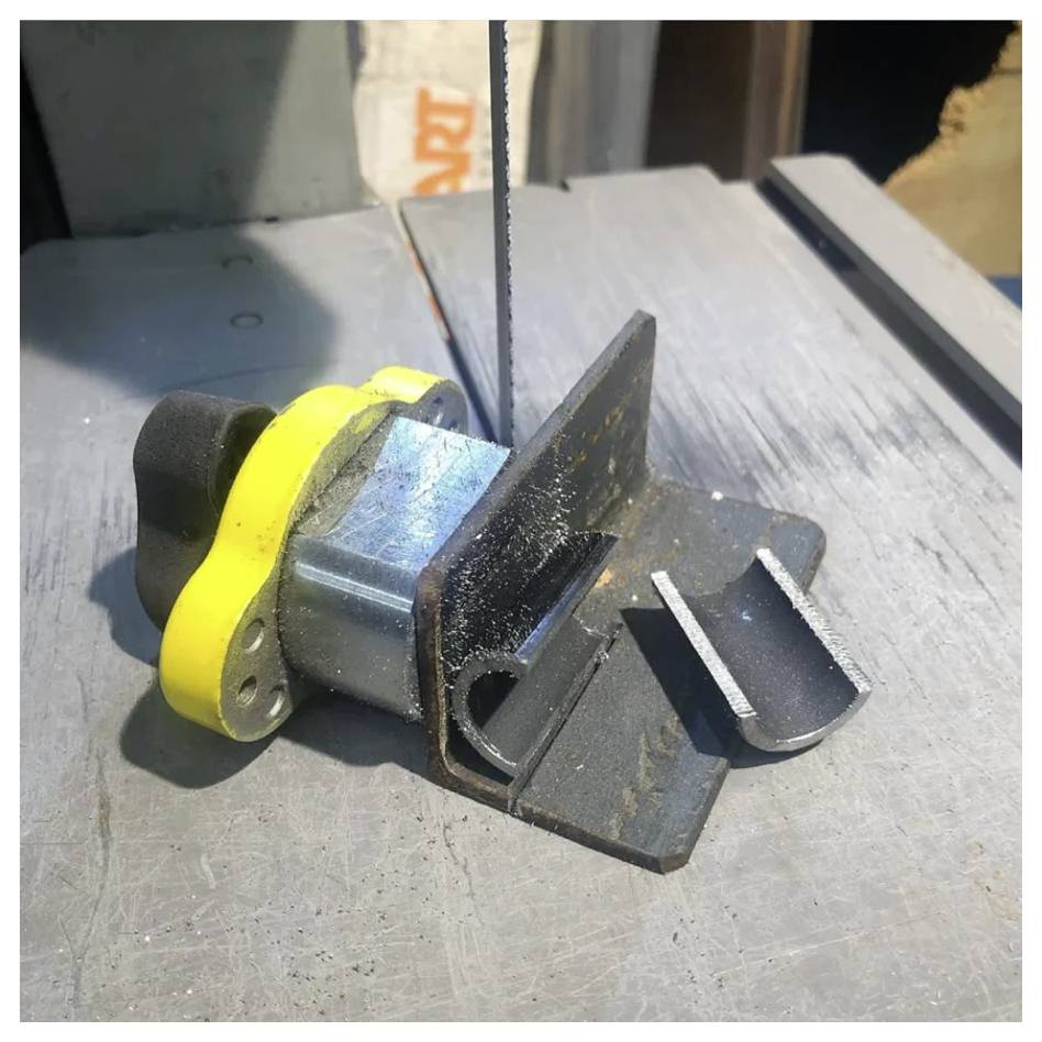 Eine Metallklemme, die einen Block festhält, wird von einer vertikalen Bandsägeblatt in einer Werkstattumgebung präzise zerschnitten.