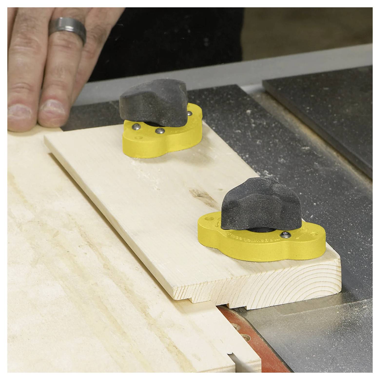 Eine Holzbearbeitungslehre mit einer gelben Basis hält ein Holzbrett sicher, während eine Hand sich darauf vorbereitet, präzise Schnitte an einer Tischkreissäge durchzuführen.