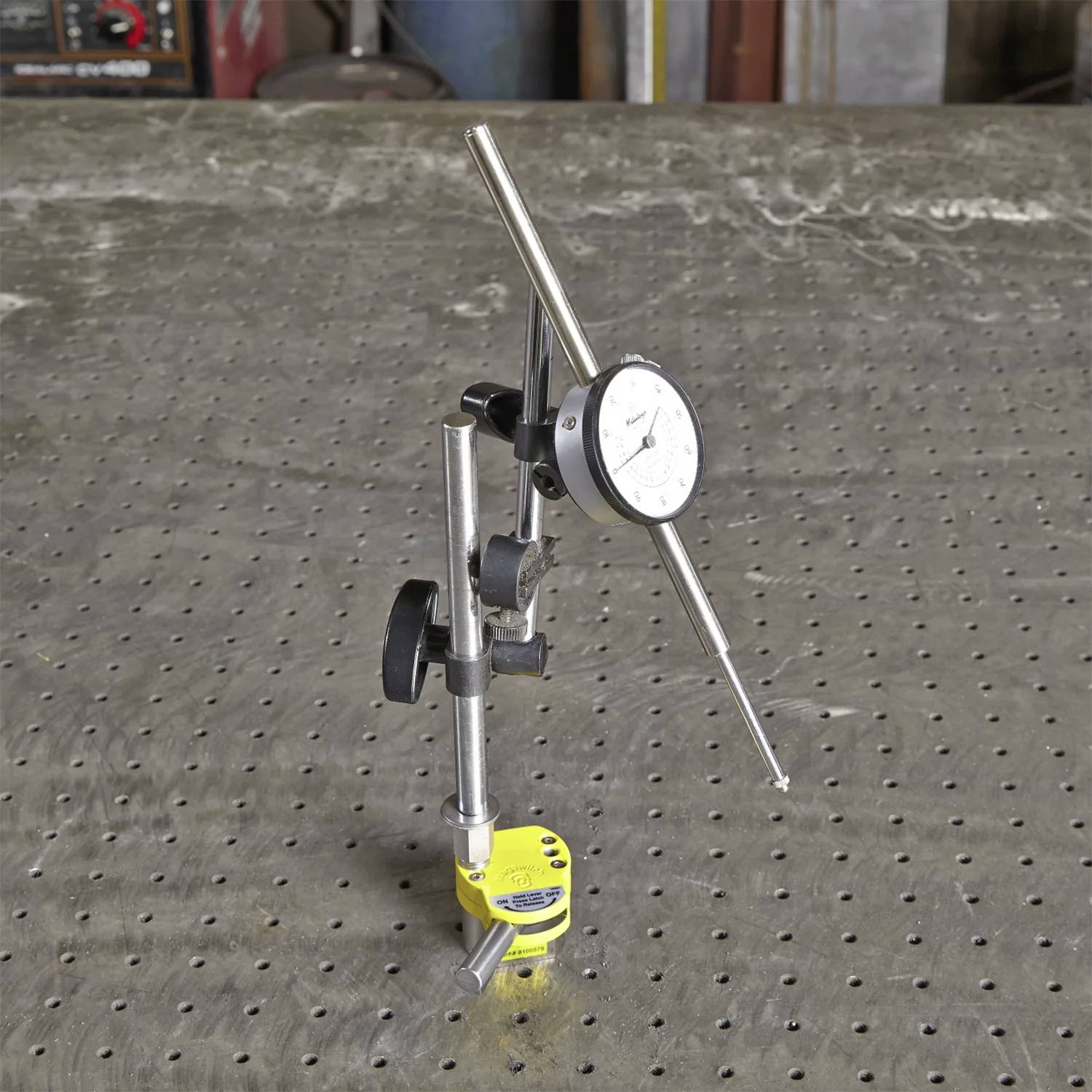 Ein Messuhrzeiger, montiert auf einer Magnethalterung, steht auf einer gelochten Metalloberfläche und wird für Präzisionsmessungen bei der Bearbeitung verwendet.