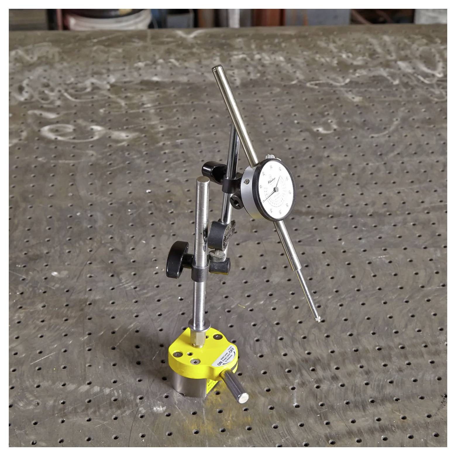 Ein Messuhr auf einer Magnethalterung wird auf einem gelochten Metalltisch positioniert, der für präzise Messungen und Ausrichtungen in technischen Aufgaben verwendet wird.