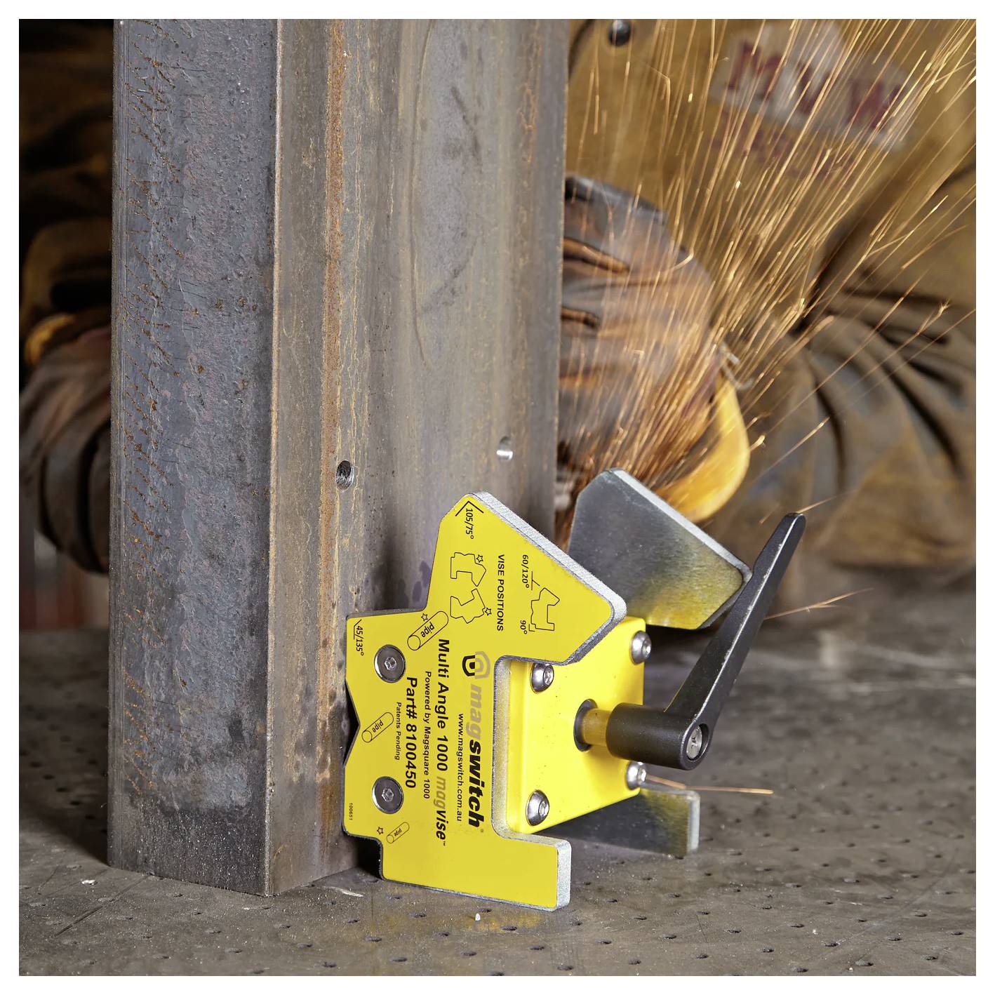 Ein magnetischer Schweißhalter befestigt ein Metallstück im rechten Winkel, während ein Operator schweißt und Funken sprühen. Sicherheitsausrüstung ist sichtbar.