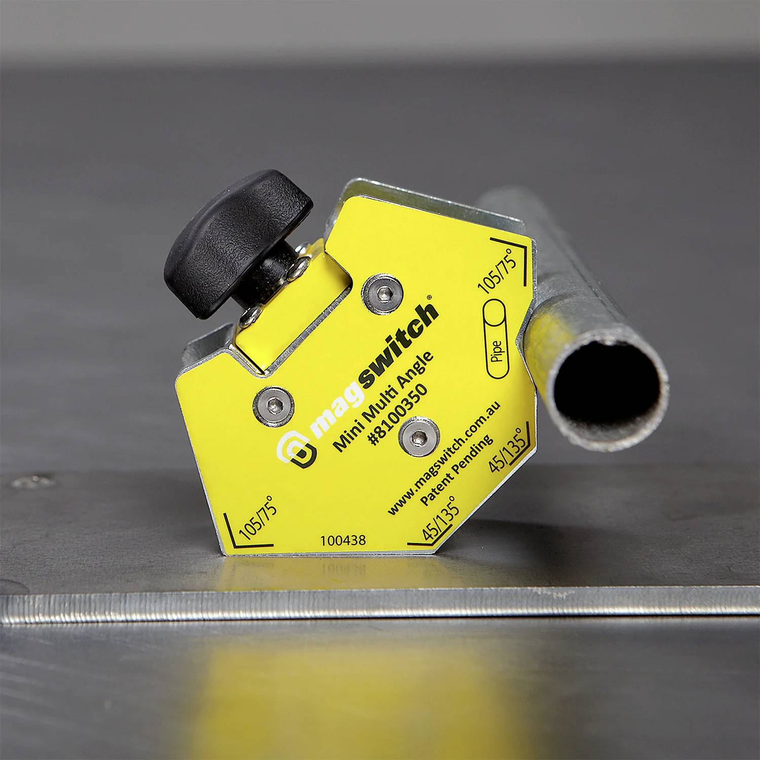 Ein gelber Magswitch Mini-Multi-Winkel-Werkzeug hält ein Metallrohr auf einer metallischen Oberfläche und wird zum Ausrichten und Festhalten von Objekten während des Schweißens verwendet.